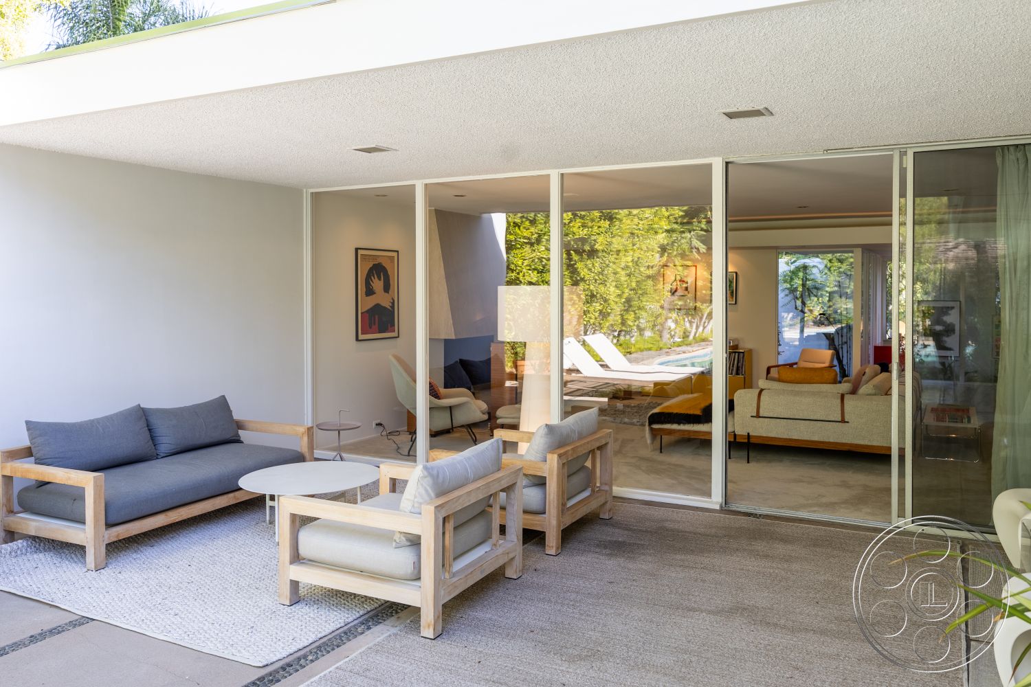 MCM 27 - neutral color palette, exterior, sliding glass doors, landscaped garden view, gathering space, woven area rug, textured wall finishes, minimalist coffee table, modern outdoor seating, exposed wood ceiling beams, concrete patio flooring, open concept living area, sunlit courtyard, wood frame furniture, low-profile modern lounge chairs