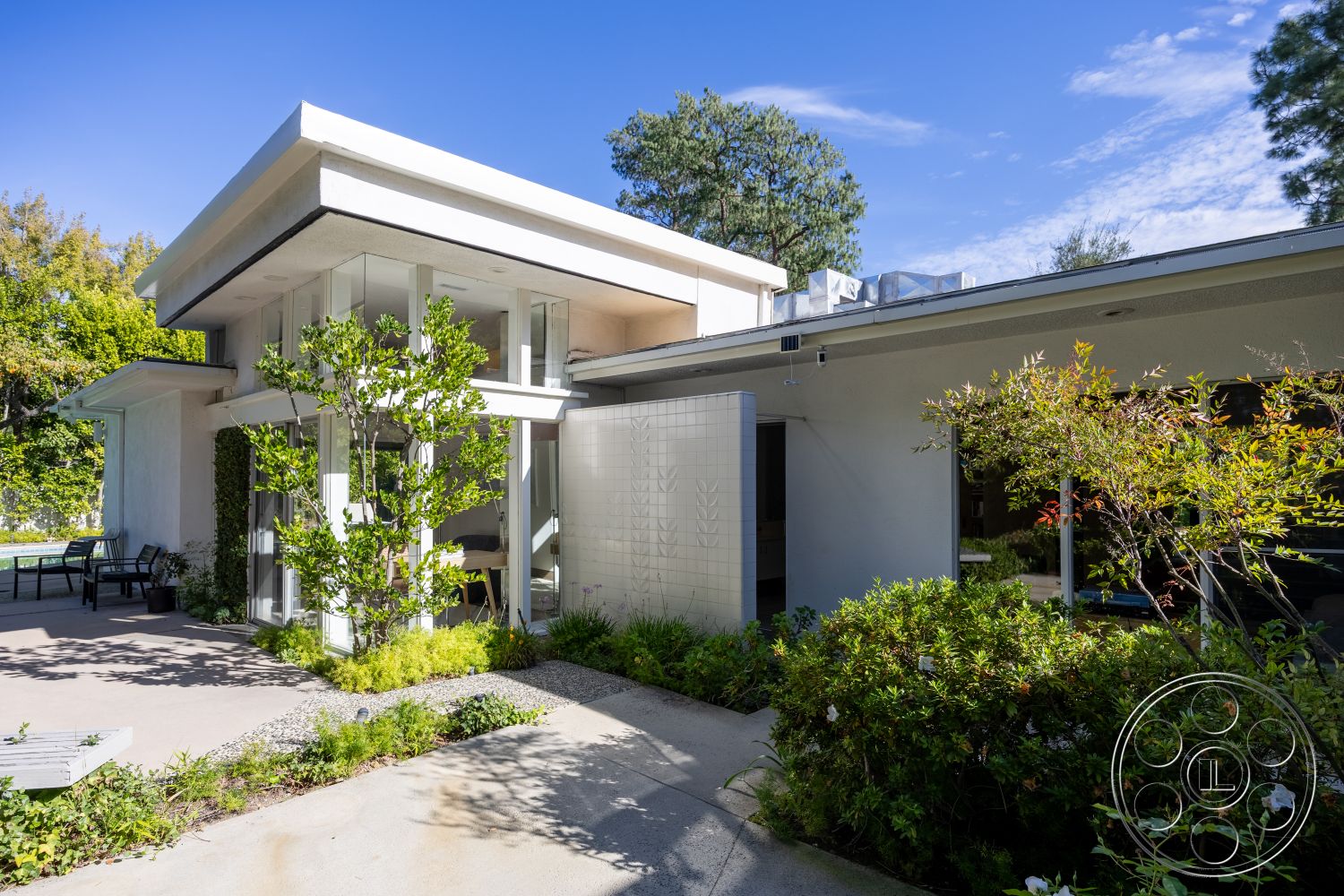 MCM 27 - exterior concrete patio floor, exterior landscaped garden, interior open concept living area, interior large glass doors, exterior flat roof design, exterior natural stone accents, exterior minimalist design elements, exterior glass window walls, exterior white stucco finish, exterior modernist architectural style, exterior sleek geometric forms, interior hardwood floor accents, interior functional outdoor seating area, interior bright natural lighting, interior lush green surroundings, interior modern landscape integration