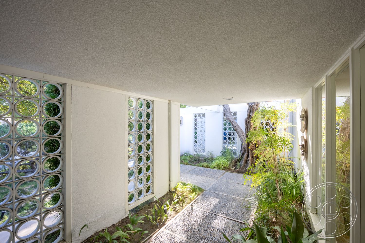 MCM 27 - exterior, modern architectural style, concrete walkway, integrated indoor-outdoor flow, mid-century modern design, landscaped garden area, natural stone garden path, textured ceiling finish, glass block windows, open-air corridor, linear plant beds, smooth stucco walls