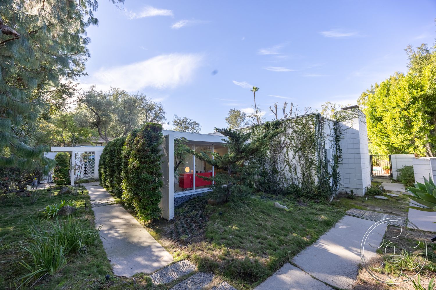 MCM 27 - large windows, lush greenery, natural wood accents, outdoor seating area, concrete pathway, exterior landscaping, inviting entrance, single-story home, modern outdoor lighting, urban garden, wooden fence, textured plaster walls, ivy-covered walls, white concrete walls, slate stone accents, Mid-Century Modern style, organic shape landscaping, decorative garden stones, city backyard setting