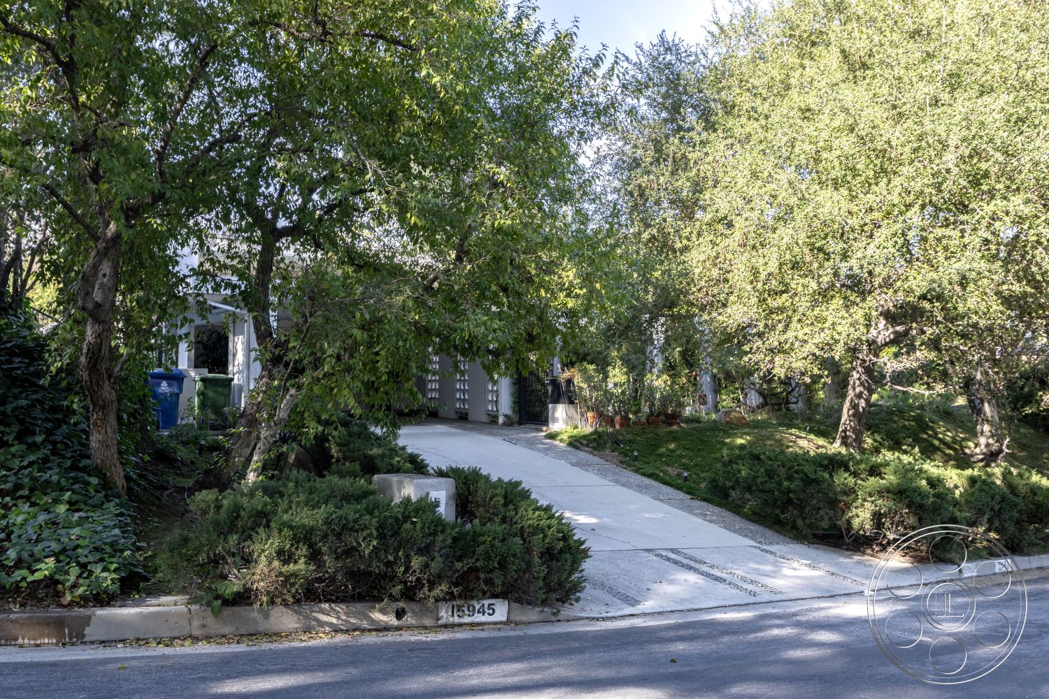 MCM 27 - suburban neighborhood, landscaped front yard, concrete walkway, open green space, exterior concrete driveway, modern architectural details, natural light filtering through trees, curved driveway design, mature trees in garden, green shrubbery border, residential home setting, impression of spaciousness