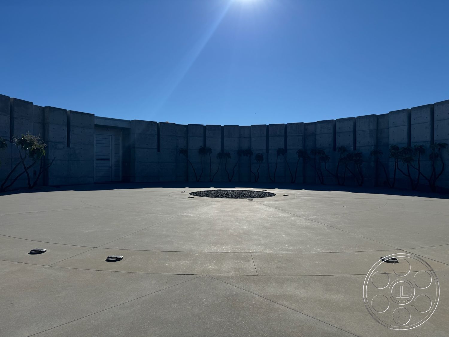 Fortress - smooth concrete surface, contemporary outdoor space, functional outdoor space, rectilinear forms, environmentally integrated design, exterior concrete patio floor, minimalist architectural design, exterior concrete walls, sunlit outdoor setting, circular concrete courtyard, low-maintenance landscaping with shrubs, modern concrete design, hardscaped garden area, integrated landscape features, stylized round planter feature, urban architectural style, focal point central composition, open-air circulation, designed for socialization and leisure