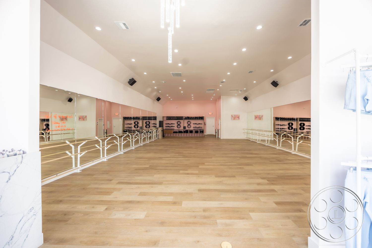 Long mirrored barre studio with warm wood flooring, white double ballet barres and a soft pink back wall at Gym 37, a boutique fitness filming location in West Hollywood
