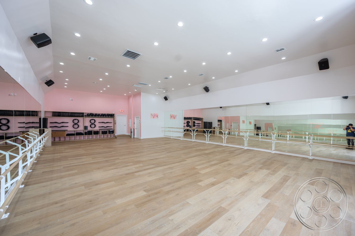 Gym 37 - open floor plan, pink accent wall, modern minimalist design, white painted walls, functional storage shelves, hardwood studio flooring, exposed ceiling with recessed lighting, mirrored wall treatment, floor-to-ceiling mirrors, modern ballet barre fixtures, dance studio interior, spacious workout area, acoustic panels for soundproofing, industrial-style ventilation ducts, dance exercise room