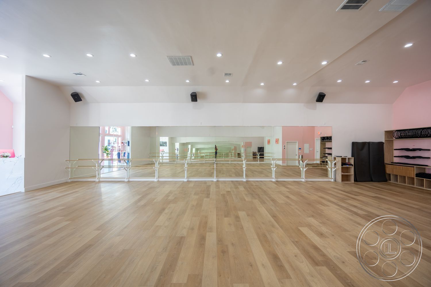 Gym 37 - white painted walls, interior dance studio with hardwood flooring, mirrored wall paneling, acoustic ceiling with recessed lighting, ballet barre railing, natural wood shelving units, neutral color palette with pink accents, spacious layout for movement, brightly lit environment, modern design with clean lines