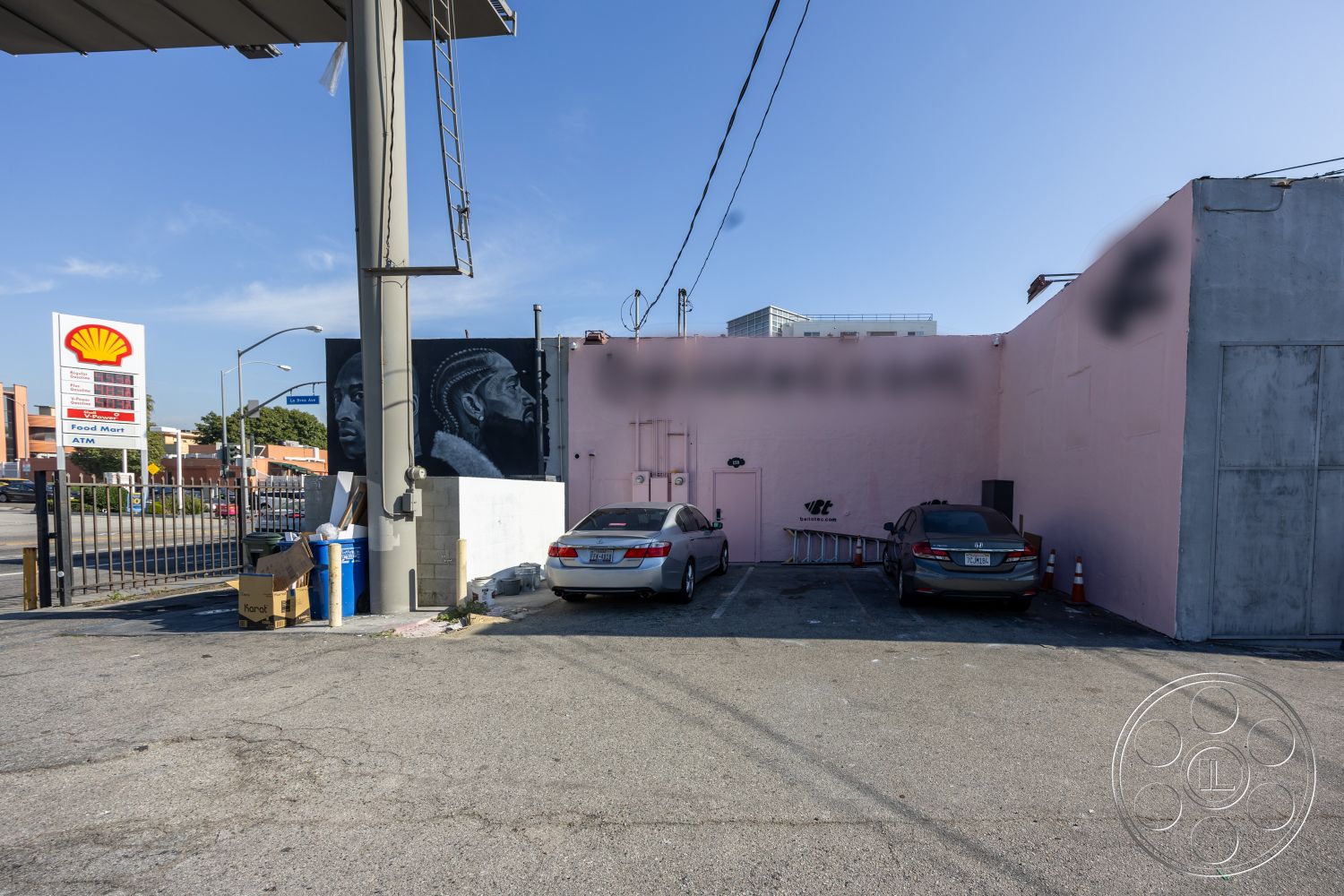 Gym 37 - exterior, asphalt surface, urban setting, commercial building, graffiti art, chain link fence, concrete parking lot, flat roof design, pink stucco wall, graffiti mural detail, steel post structure, surrounding commercial district, dimensional signage, paved access road, utility connections visible, littered refuse area, ambient street lighting