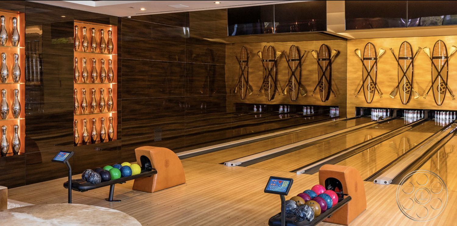 Modern 518 - game room, polished wood flooring, wood panel accent wall, sleek contemporary design, ambient LED lighting, luxury recreational space, interior bowling alley, modern bowling lanes, built-in bowling ball racks, high-gloss ceiling finishes, decorative bowling pin display, themed wall decor with vintage skis, multicolored bowling balls, customized entertainment area, open layout recreational design