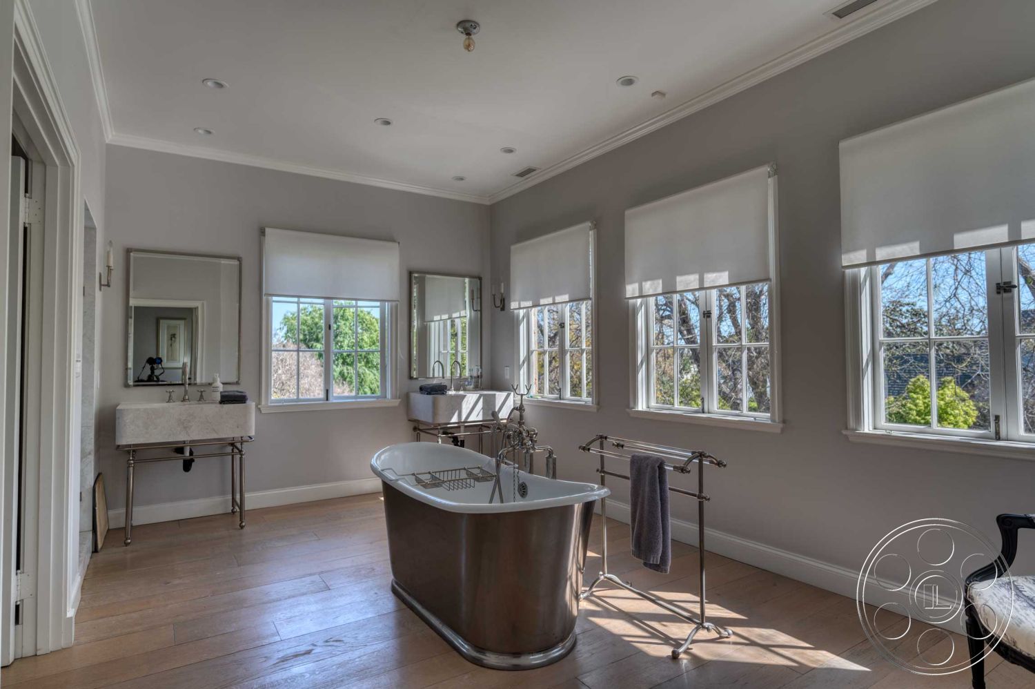 The French Chateau - minimalist design, open space layout, landscape view, dual vanities, rectangular windows, contemporary bathroom style, chrome faucet fixtures, freestanding soaking tub, natural light exposure, light gray painted walls, calm and serene atmosphere, wood plank bathroom flooring, marble sink vanity, mirrored bathroom cabinets, roller shades window treatments, brushed nickel towel rack, white crown molding details