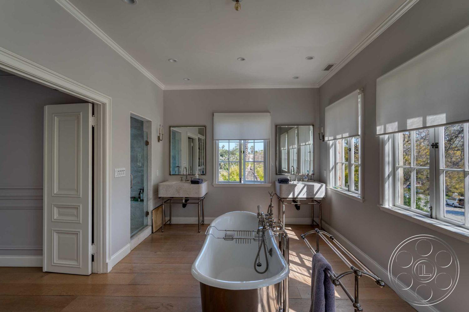 The French Chateau - hardwood flooring, minimalist aesthetic, freestanding bathtub, glass shower enclosure, framed mirrors, natural light illumination, interior bathroom, chrome faucet fixtures, luxury bathroom design, large window views, gray painted walls, decorative baseboards, modern vanity sink, double window treatments, door with detailed paneling