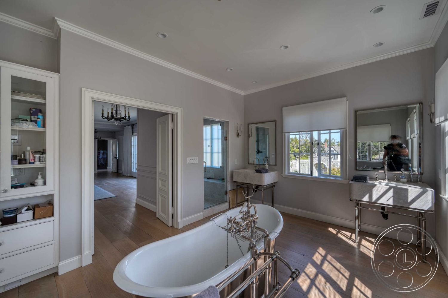 The French Chateau - neutral color palette, glass shower enclosure, modern minimalist design, decorative molding details, interior bathroom, large windows with natural light, hardwood bathroom flooring, quirky chandelier lighting, light gray painted walls interior, freestanding white tub, double vanity with marble countertops, younger urban home, transitional bathroom style, exquisite chrome fixtures, light-filled contemporary space, compact organized storage cabinets, window treatments with shades, luxurious bathroom amenities, master bathroom suite, serene spa-like atmosphere