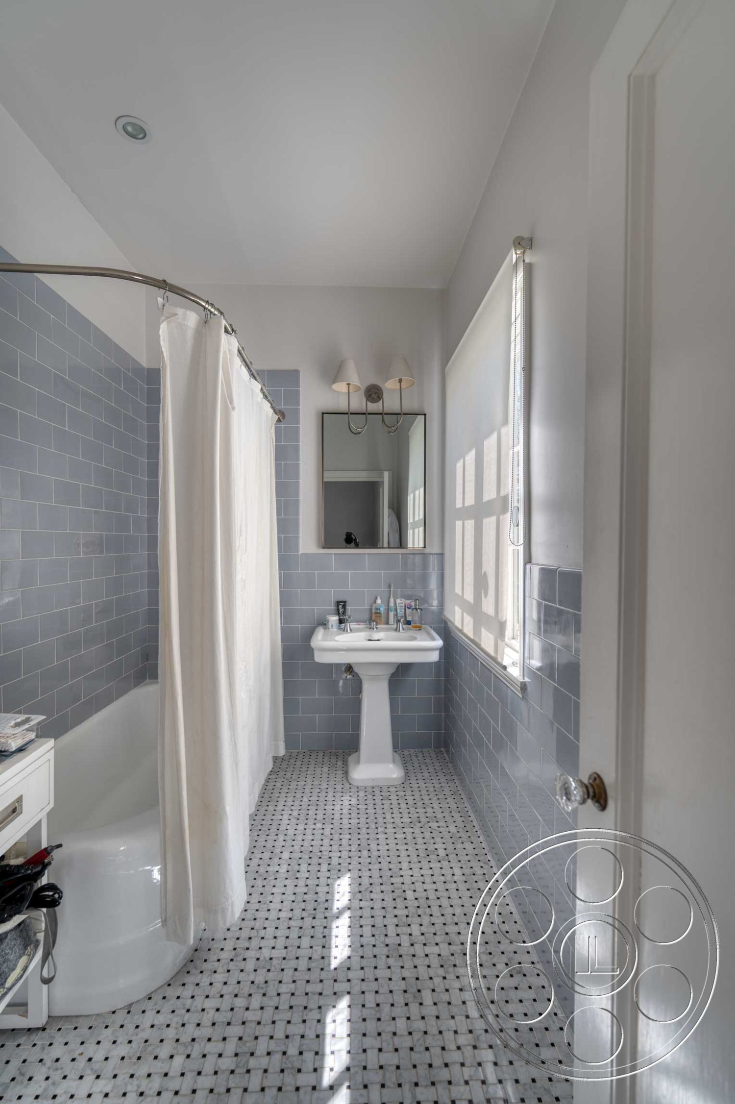 The French Chateau - neutral color palette, clean lines, minimalist design, modern light fixtures, natural light from window, interior bathroom, curved shower curtain rod, white ceramic bathtub, contemporary bathroom styling, gray subway tile walls, porcelain pedestal sink, black and white mosaic tile flooring, shower area with curtain, white window treatments