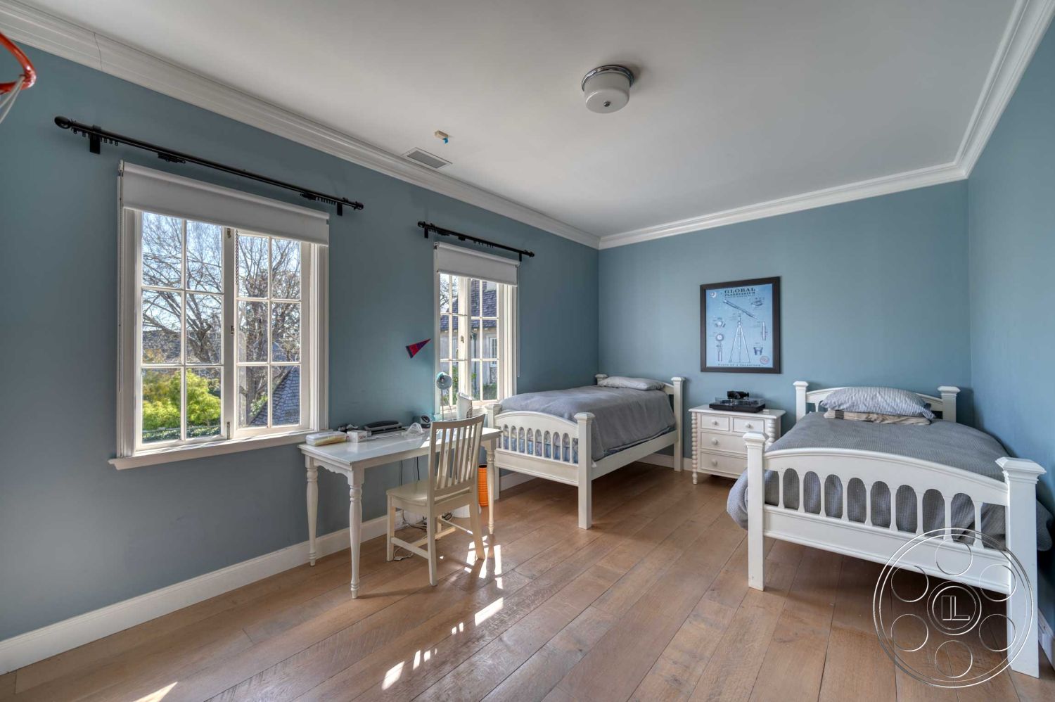 The French Chateau - decorative wall art, natural light from large windows, interior bedroom, hardwood bedroom floors, blue painted walls, white crown molding details, double-hung windows with white trim, white wooden bed frames, bedroom with two twin beds, contemporary desk with white finish, simple white chair
