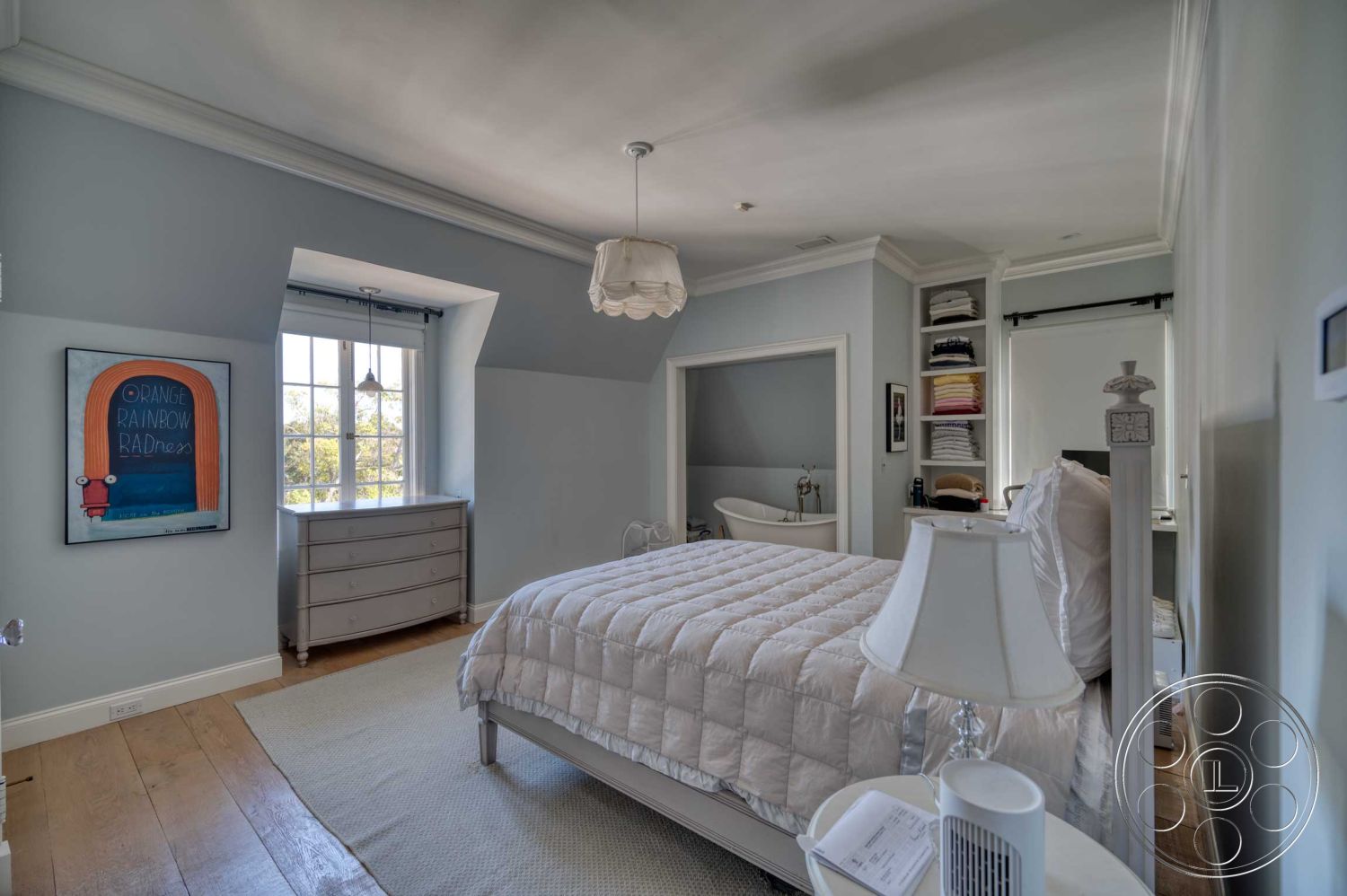 The French Chateau - freestanding bathtub, vaulted ceiling, master bedroom, glass window treatments, hardwood bedroom floors, white painted walls, exposed wood trim details, built-in storage shelves, soft beige area rug, art deco ceiling light fixture