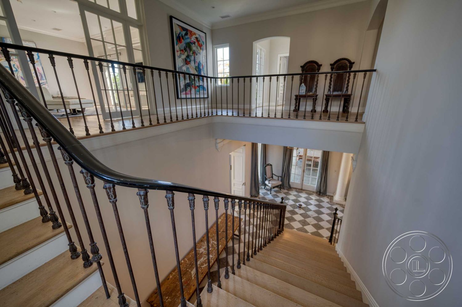 The French Chateau - light hardwood flooring, artistic wall decor, high vaulted ceiling, spacious entryway, natural light-filled space, open concept living area, elegant chandelier lighting, metal stair railings, gray painted walls, interior staircase, textured plaster wall details, curved staircase design, checkerboard tile flooring, floating wooden stairs, dark wood handrail, polished marble landing, traditional floor-to-ceiling windows, modern artwork display