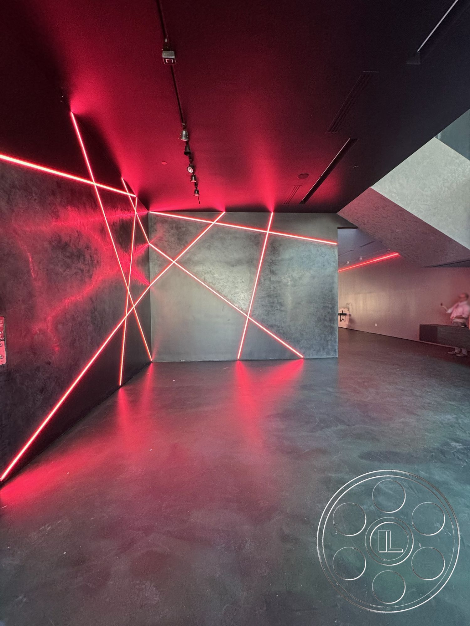 Sunset Studio - open layout, concrete floor, textured wall finish, interior space, minimalistic decor, industrial design elements, LED lighting features, geometric wall patterns, high-contrast color scheme, modern architectural details, neon light accents, dark ceiling panels, abstract wall design, dimly lit environment, artistic contemporary style