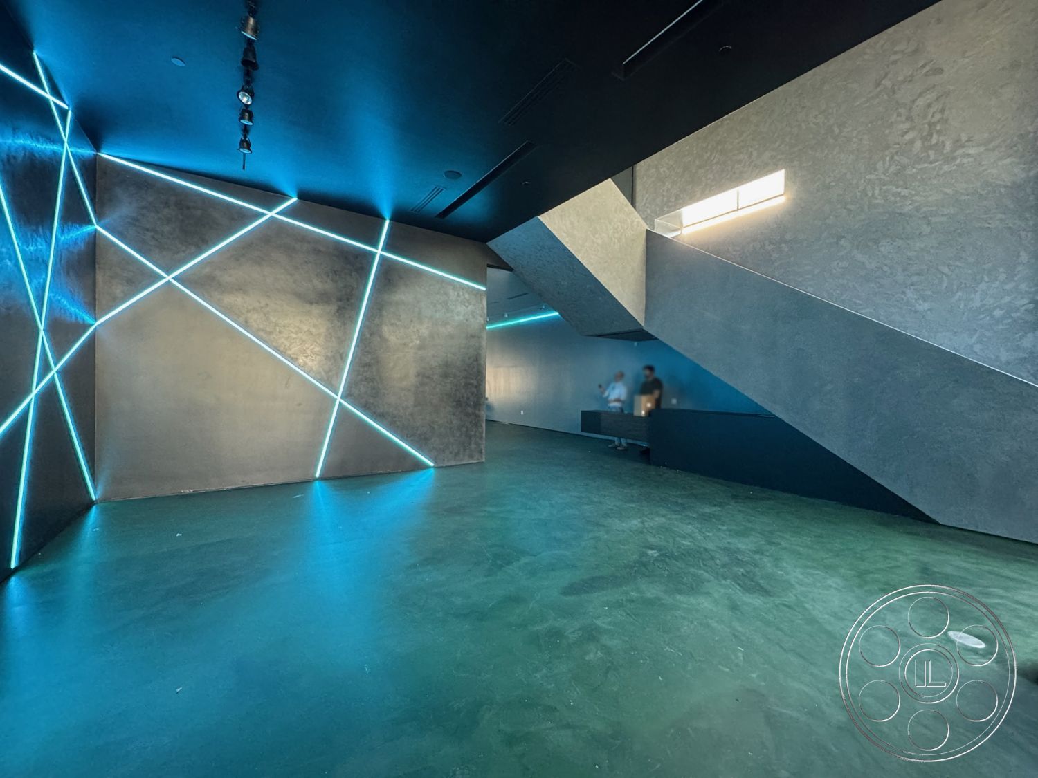 Sunset Studio - neutral color palette, minimalist aesthetic, polished concrete floor, open floor plan, exposed concrete walls, industrial design elements, modern architectural style, sloped ceiling, geometric wall design, black ceiling panels, LED lighting accent details, angular staircase design