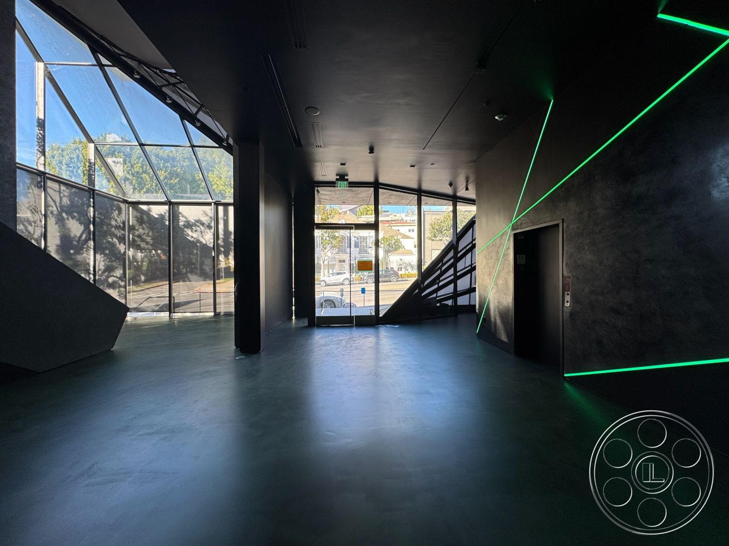 Sunset Studio - polished concrete flooring, large glass windows, interior space, urban setting, contemporary architectural style, natural light illumination, steel stair railings, clean lines design, angular glass architecture, black textured wall finish, geometric lighting accents, modern open layout, corner view entrance