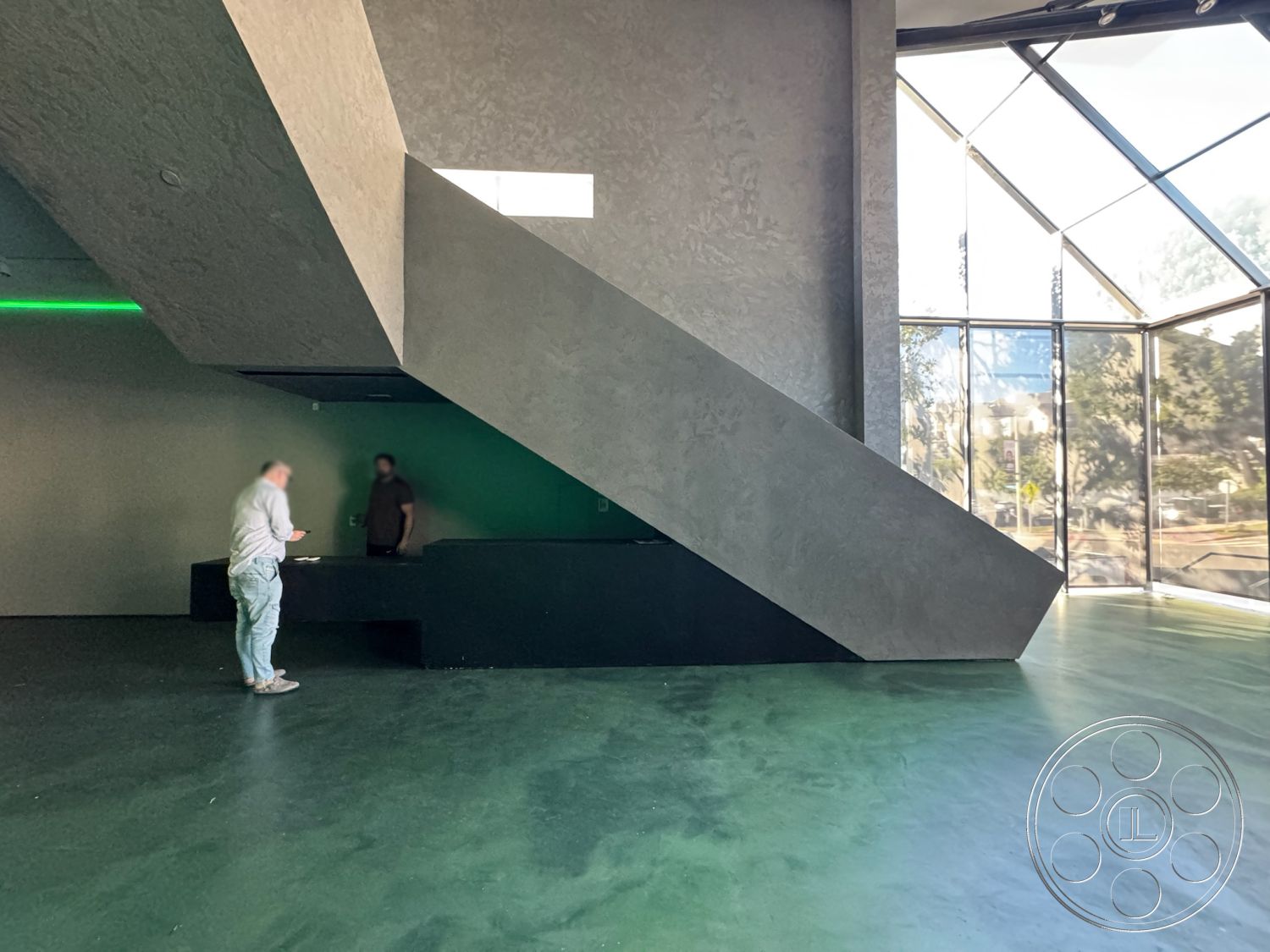 Sunset Studio - neutral color palette, minimalist design elements, interior space, polished concrete floors, black cabinetry, steel frame structure, industrial aesthetic, low-profile furniture, open floor plan layout, floor-to-ceiling glass windows, natural light sources, contemporary architectural details, urban environment setting, exposed concrete wall finish, modern geometric shapes, angular roofline, sloping concrete staircase, integrated lighting systems