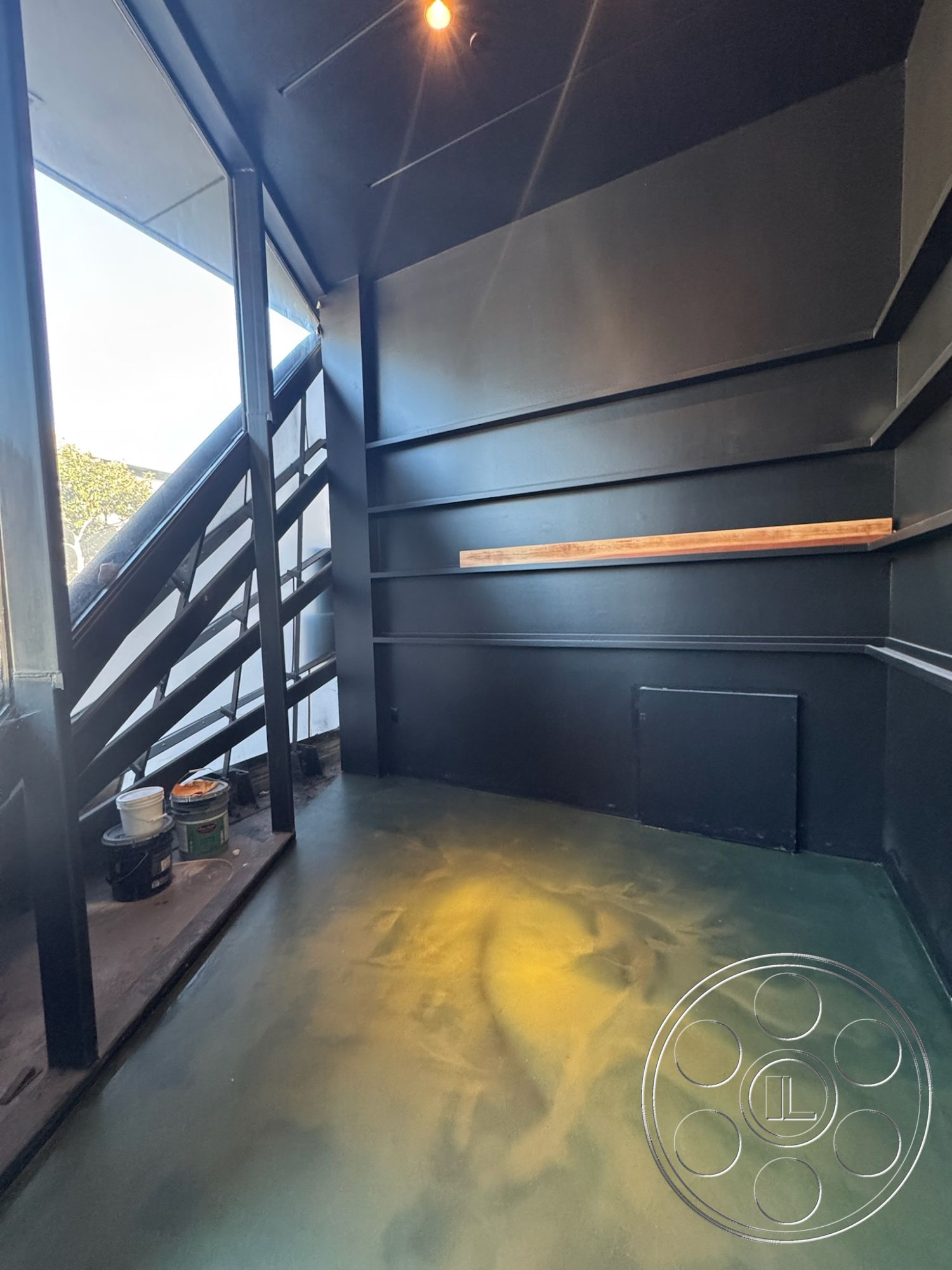 Sunset Studio - minimalist aesthetic, interior space, smooth concrete flooring, exposed ceiling structure, open staircase design, glass window wall, black wall treatment, industrial style stair railings, wood bar counter, sloping wall shapes