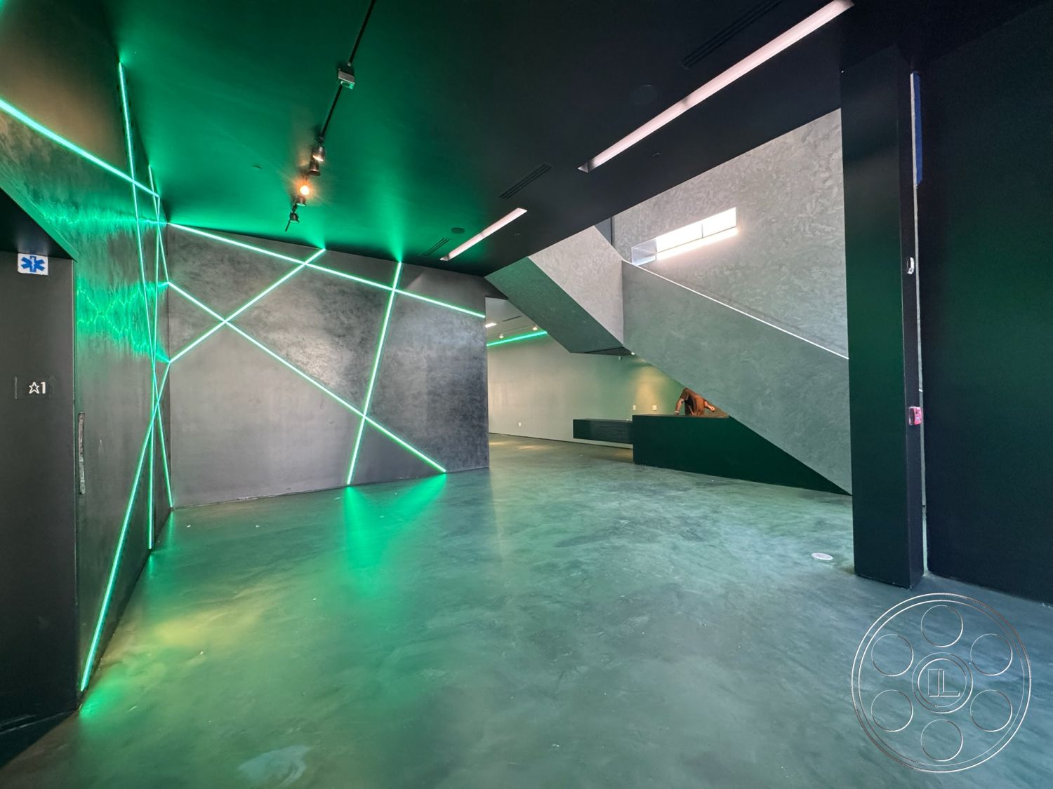 Sunset Studio - contemporary design, polished concrete floor, black accent wall, exposed structural elements, industrial interior, linear LED ceiling lighting, textured dark plaster walls, angular staircase, neon green wall lighting, modern architectural detailing