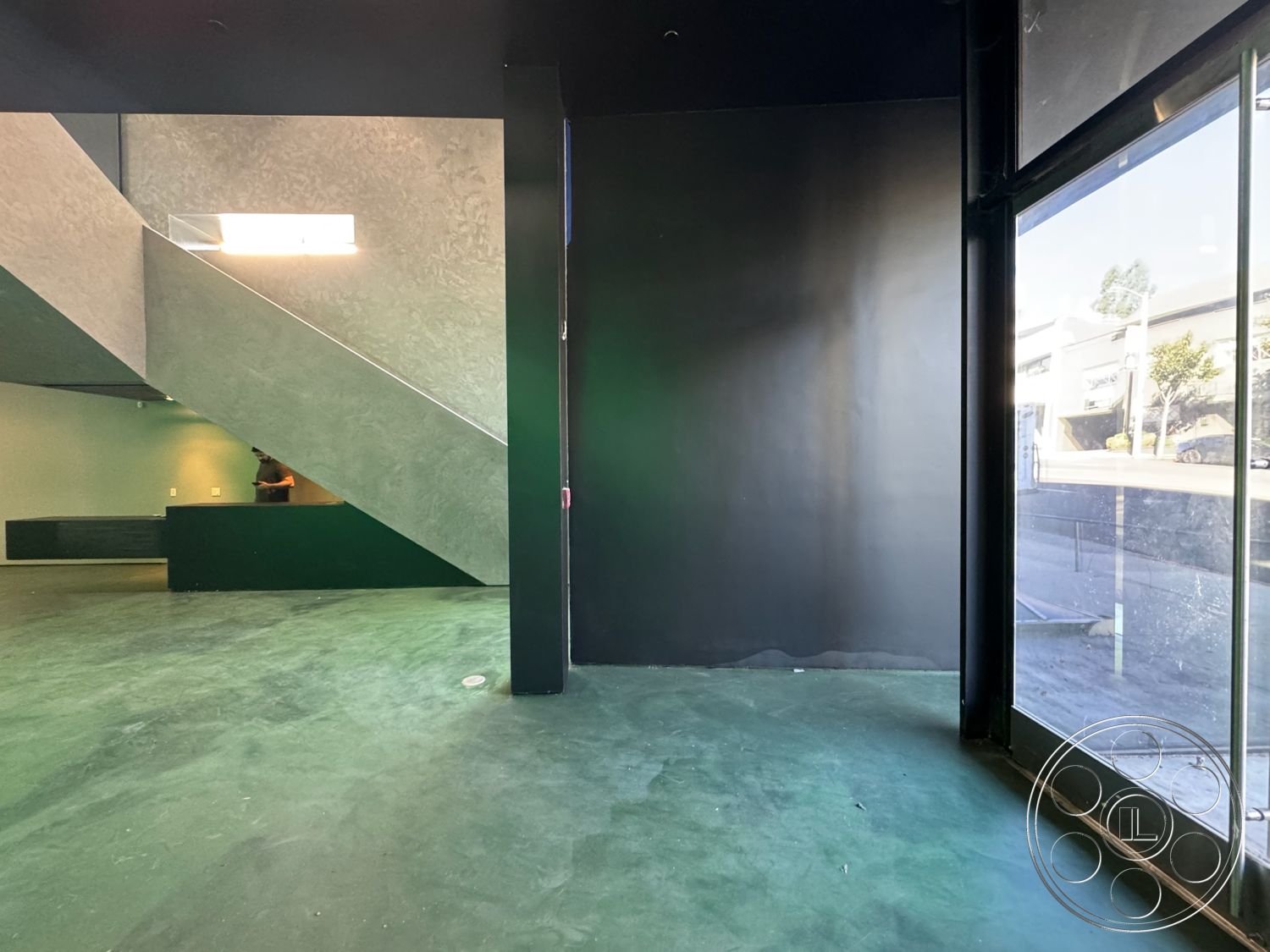 Sunset Studio - neutral color palette, open space layout, minimalistic design elements, interior concrete flooring, modern architectural details, glass storefront windows, urban interior setting, industrial style lighting fixtures, polished concrete surface, exposed concrete staircase, concrete structural walls, black painted accent wall, large glass panels for natural light