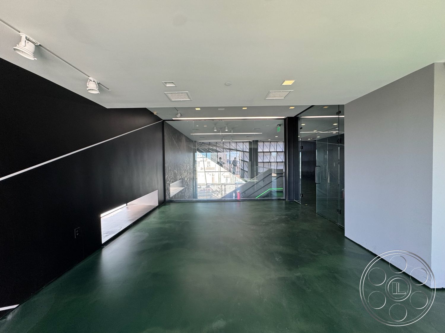 Sunset Studio - open concept layout, exposed concrete walls, minimalist interior design, track lighting fixtures, urban interior setting, industrial style elements, modern glass door, angular architectural forms, polished concrete finish, green resin flooring, floor-to-ceiling glass partition walls, indoor stair railings, smooth finished ceiling, sharp geometric shapes