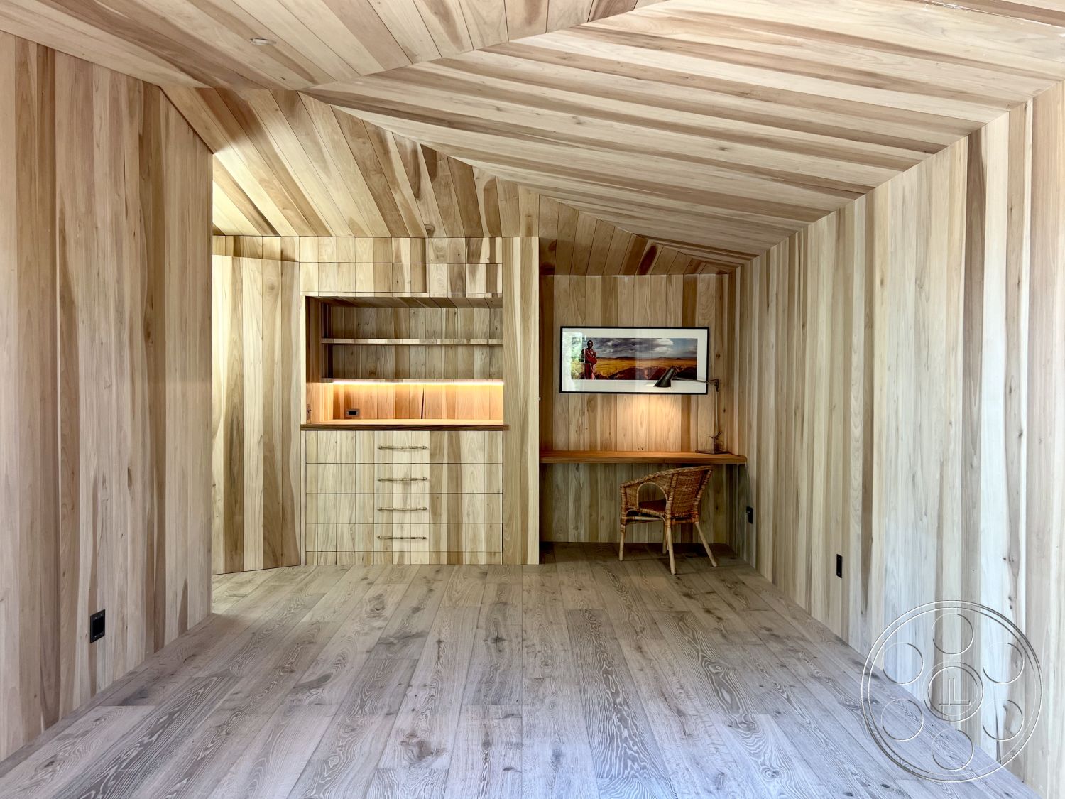 Zen Garden - light hardwood flooring, soft ambient lighting, contemporary interior style, open and airy space, built-in wooden cabinets, interior wood panel walls, interior tongue-and-groove wood ceiling, natural wood desk area, rustic accent chair, minimalistic wall decor, streamlined cabinetry design, angled wall design