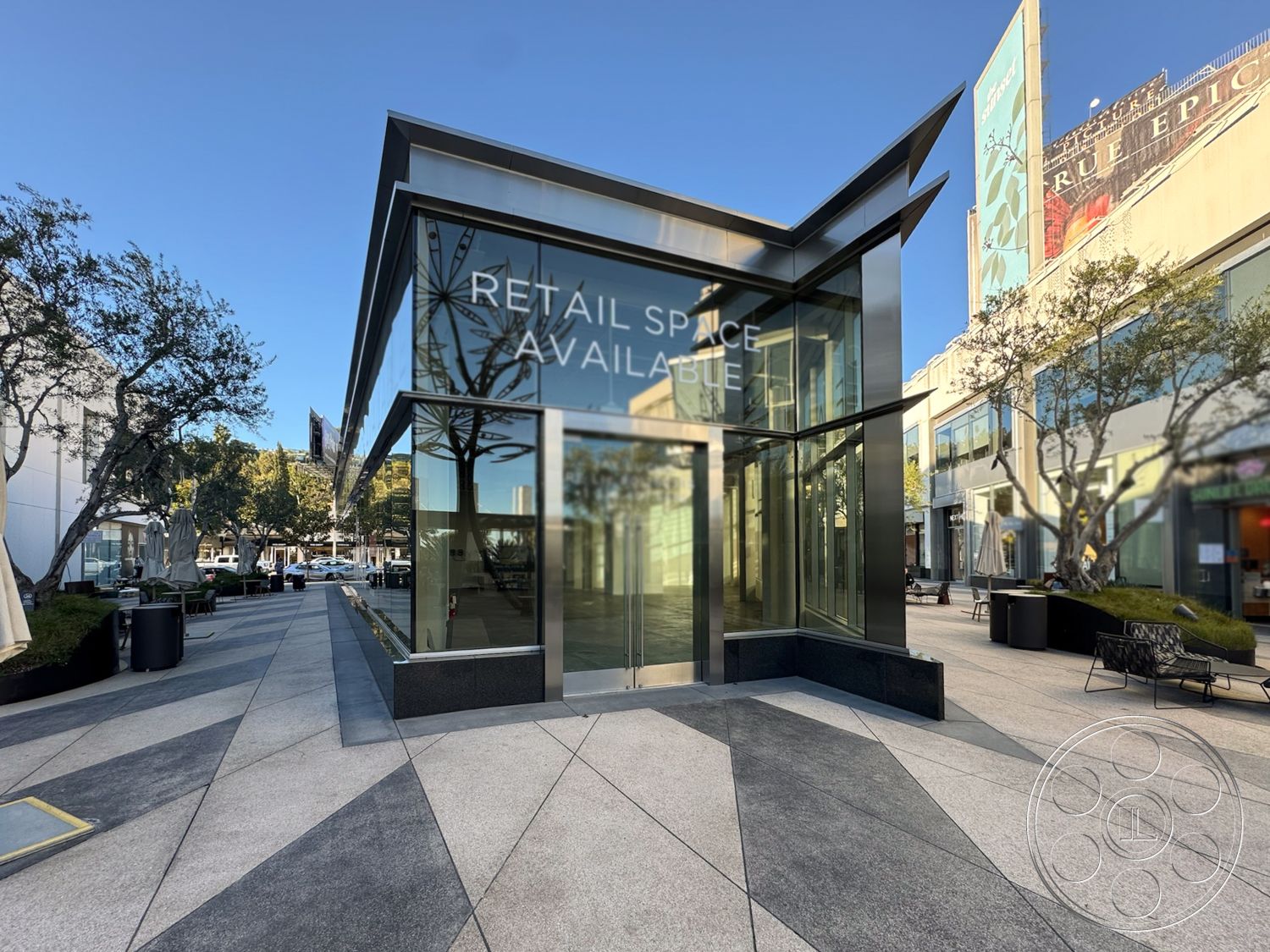 Sunset Storefront - paved walkway, environmentally friendly design, exposed structural elements, overhanging roof eaves, surrounding urban environment, landscape planters, open public space, contemporary commercial space, metal roof details, textured stone base, landscaped outdoor seating area, concrete plaza flooring, large panoramic windows, glass storefront exterior, angular modern architecture, triangular window shapes, steel structural framework, flat panel signage, urban retail setting, outdoor seating arrangements