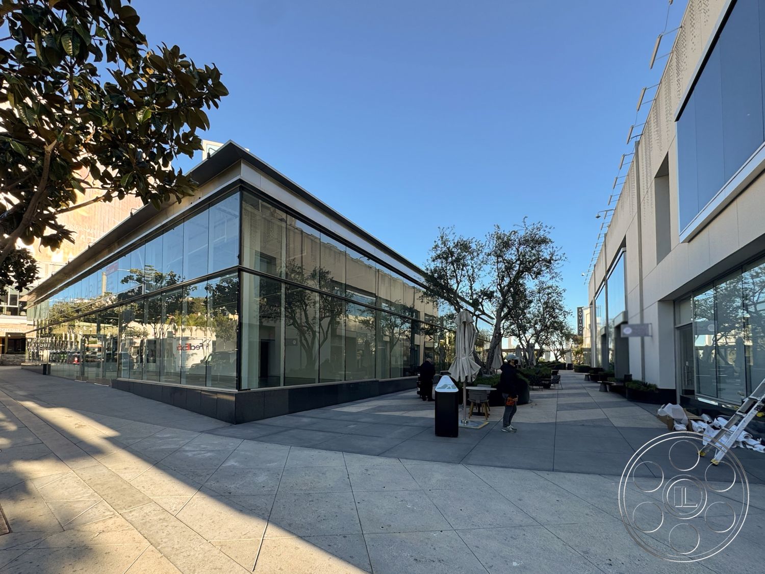 Sunset Storefront - modern architectural style, exposed structural elements, flat roof design, floor-to-ceiling glass windows, exterior glass facade, urban commercial setting, rectangular courtyard layout, reflective glass surfaces, landscaped planter beds, black granite base, polished concrete pavers, integrated outdoor seating areas, framed structural supports, entryway awning, city streetscape