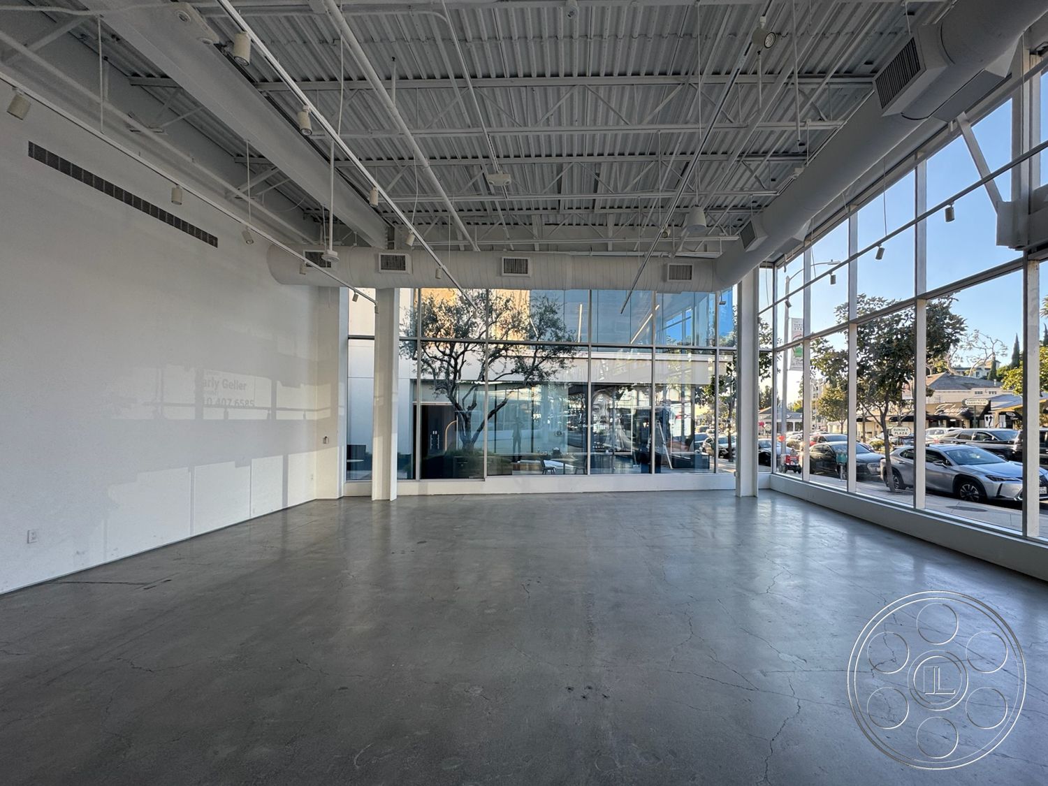 Sunset Storefront - neutral color palette, open floor plan, minimalist design elements, large glass windows, city street view, contemporary interior, white painted walls, natural light-filled environment, steel structural columns, urban commercial space, exposed polished concrete floor, industrial-style ceiling with exposed ductwork, high ceiling with track lighting, flexible layout for various uses