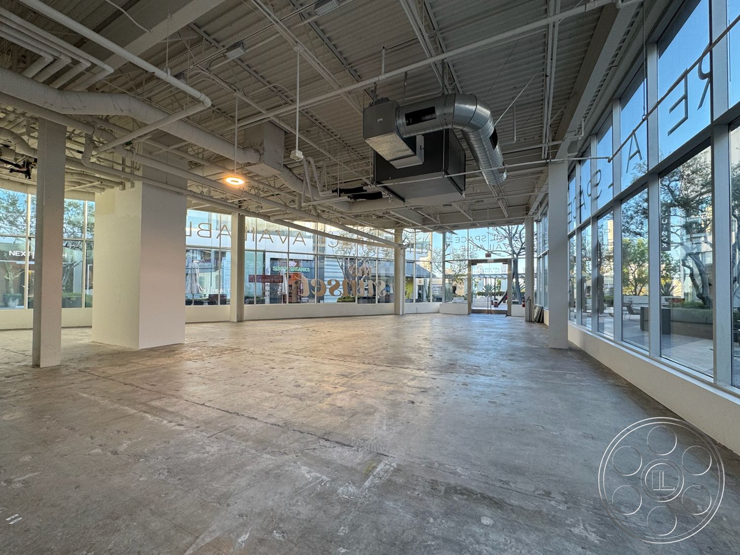 Sunset Storefront - neutral color palette, open floor plan, urban setting, commercial space, exposed concrete floor, minimalist design aesthetic, white painted walls, natural light-filled environment, industrial style interior, large glass storefront windows, steel ceiling beams, dropped ceiling with air ducts, suburban commercial area, ground-level accessibility