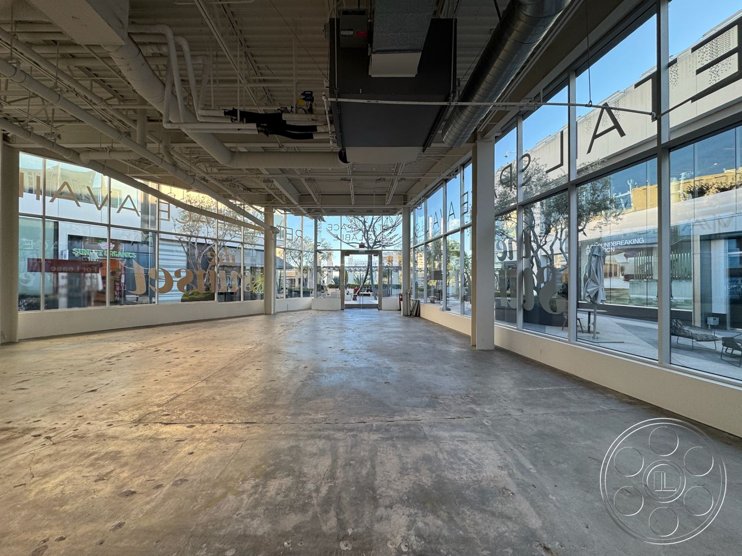 Sunset Storefront - modern lighting fixtures, exposed concrete floor, accessible entryway, minimalist architectural design, urban setting with street view, commercial space interior, large glass storefront windows, neutral color palette walls, open-plan interior, industrial-style ceiling with exposed ductwork, polished concrete flooring application, high ceiling with suspended lighting, commercial retail layout, flexible space for multi-functional use