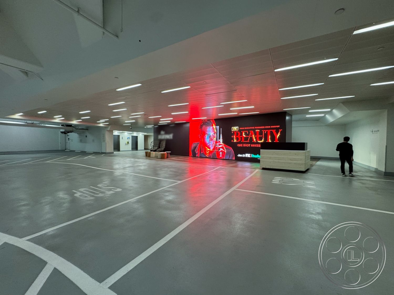 Sunset Storefront - open layout, polished concrete flooring, urban setting, recessed ceiling lights, white painted walls, modern reception desk, industrial ceiling lights, large digital display wall, exterior parking garage space, accessibility signage, clear line markings for parking, stop signage, commercial building environment