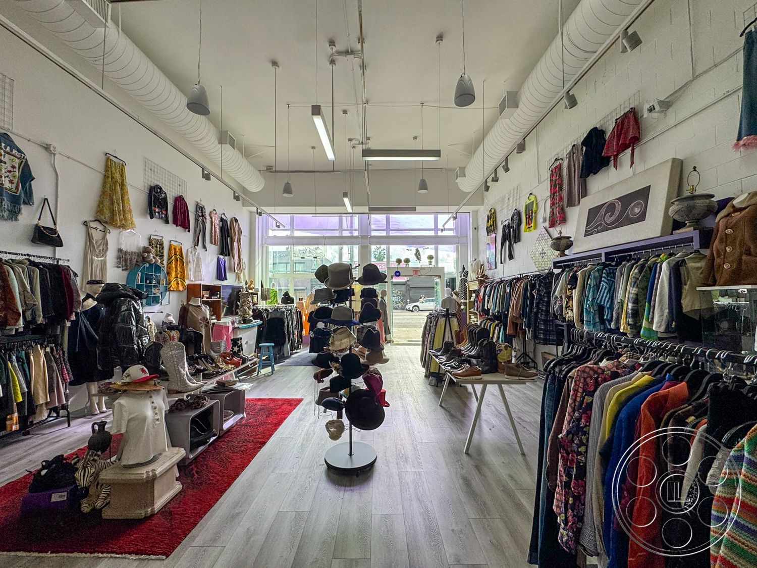 Melrose Store - textured wall art, open concept layout, modern pendant lighting, soft area rug, laminate wood flooring, white painted walls, exposed ductwork ceiling, urban street view, interior retail space, bright LED ceiling lights, multi-level clothing displays, window front display area, vintage clothing racks, faux animal skin seating, colorful clothing selection, accessory display table, sustainable fashion retail, stylistic visual merchandising