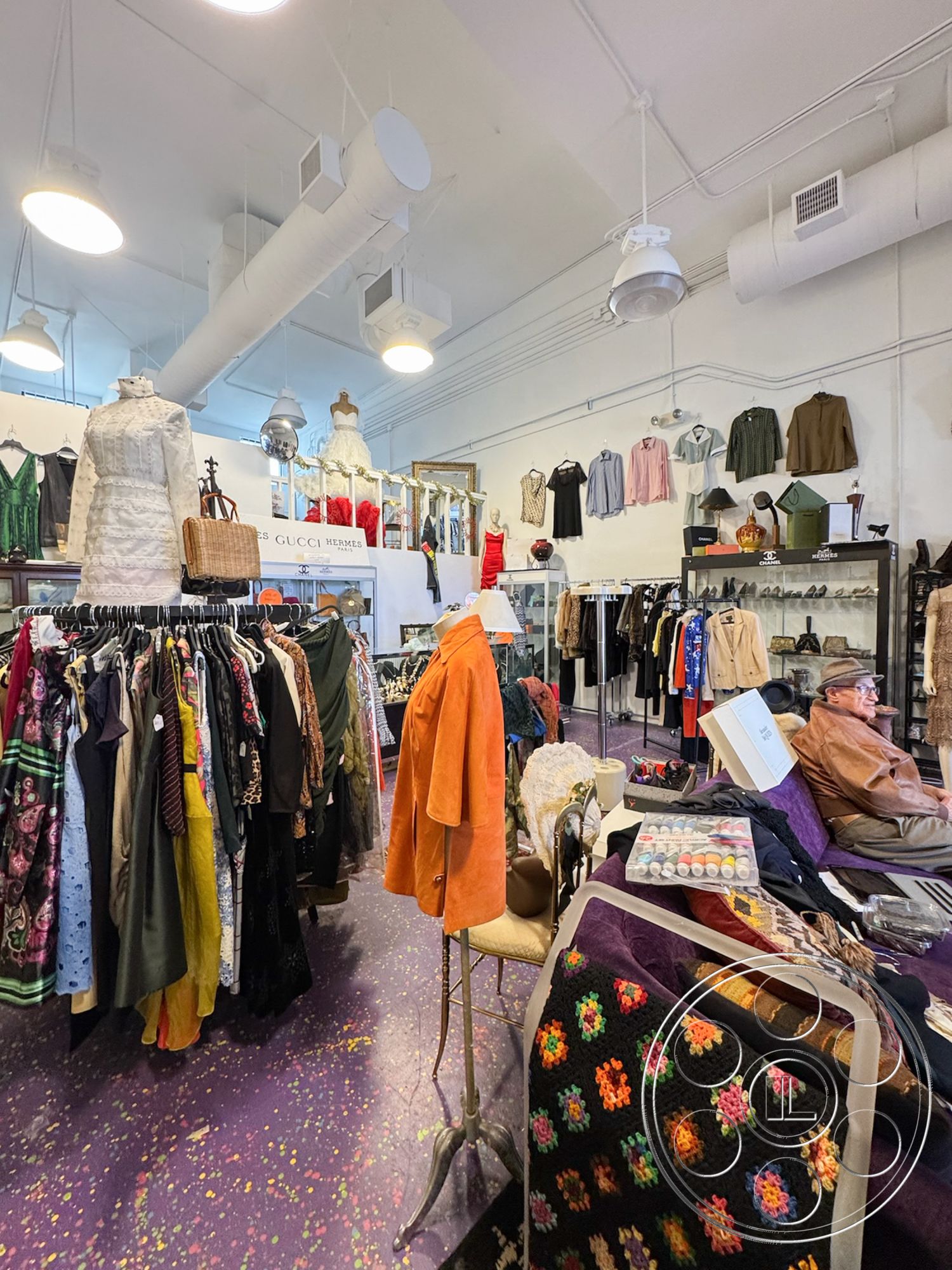 Melrose Store - wooden shelving units, open layout design, decorative wall mirror, interior clothing store, casual shopping environment, purple speckled flooring, exposed duct ceiling, brass hanging light fixtures, retail display racks, vintage clothing assortment, seating area with upholstered chair, mannequins in vintage dresses, wool knit blankets, clothing hangers with various apparel, accessory display cases