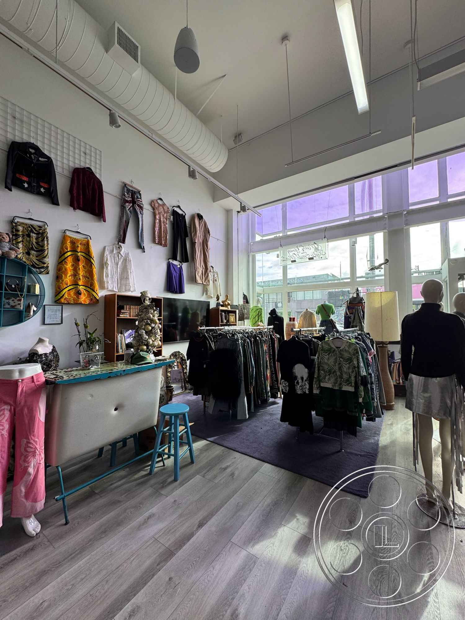 Melrose Store - open layout, urban setting, mid-century modern furniture, comfortable seating area, laminate wood flooring, white painted walls, natural light flooding space, large glass storefront windows, modern wall art, interior retail space, vintage clothing racks, casual shopping environment, dropped ceiling with exposed ductwork, creative clothing displays, soft purple ambient lighting, colorful clothing items, functional display shelving, fashion boutique, merchandise presentation area