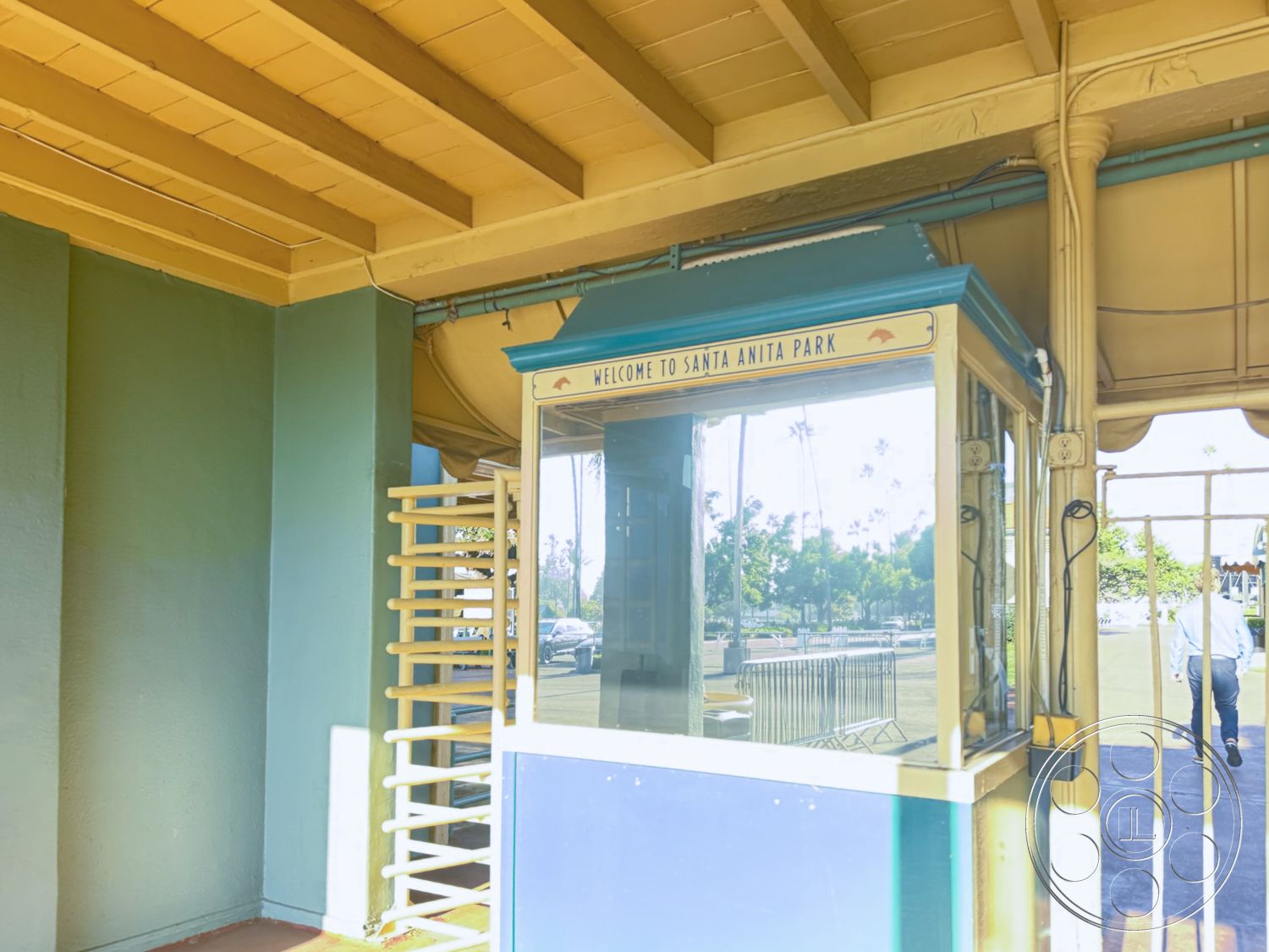 Arcadia Race Track - exterior, glass windows, open-air structure, concrete sidewalk, decorative molding details, urban park setting, clear sky backdrop, painted wood siding, metal ticket booth, brightly colored trim, art deco architectural style, landscape view of palm trees, casual visitor entry area