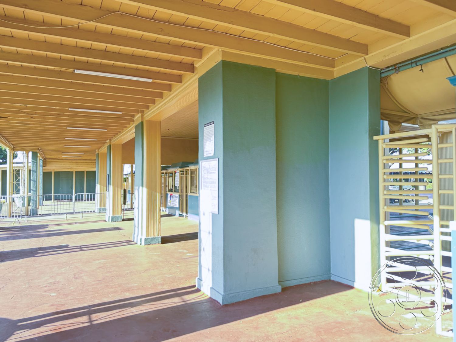 Arcadia Race Track - exterior, concrete floor, outdoor seating area, industrial design, open-air space, modern architectural style, light blue walls, textured wall treatment, minimalistic design elements, structural support beams, wood beam ceiling, smooth concrete base, green painted columns, natural light-filled area, covered communal space