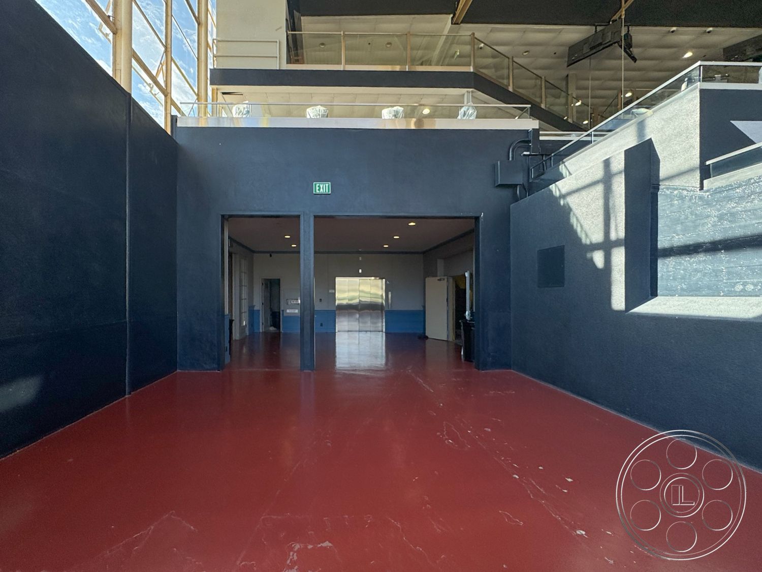 Arcadia Race Track - exterior, open layout, contemporary design elements, double door entry, black painted walls, glass storefront windows, high ceiling with exposed metal beams, modern architectural detailing, red epoxy flooring, interior space with natural lighting, tile baseboards, industrial style features, high-traffic commercial area, clear view of outdoor space