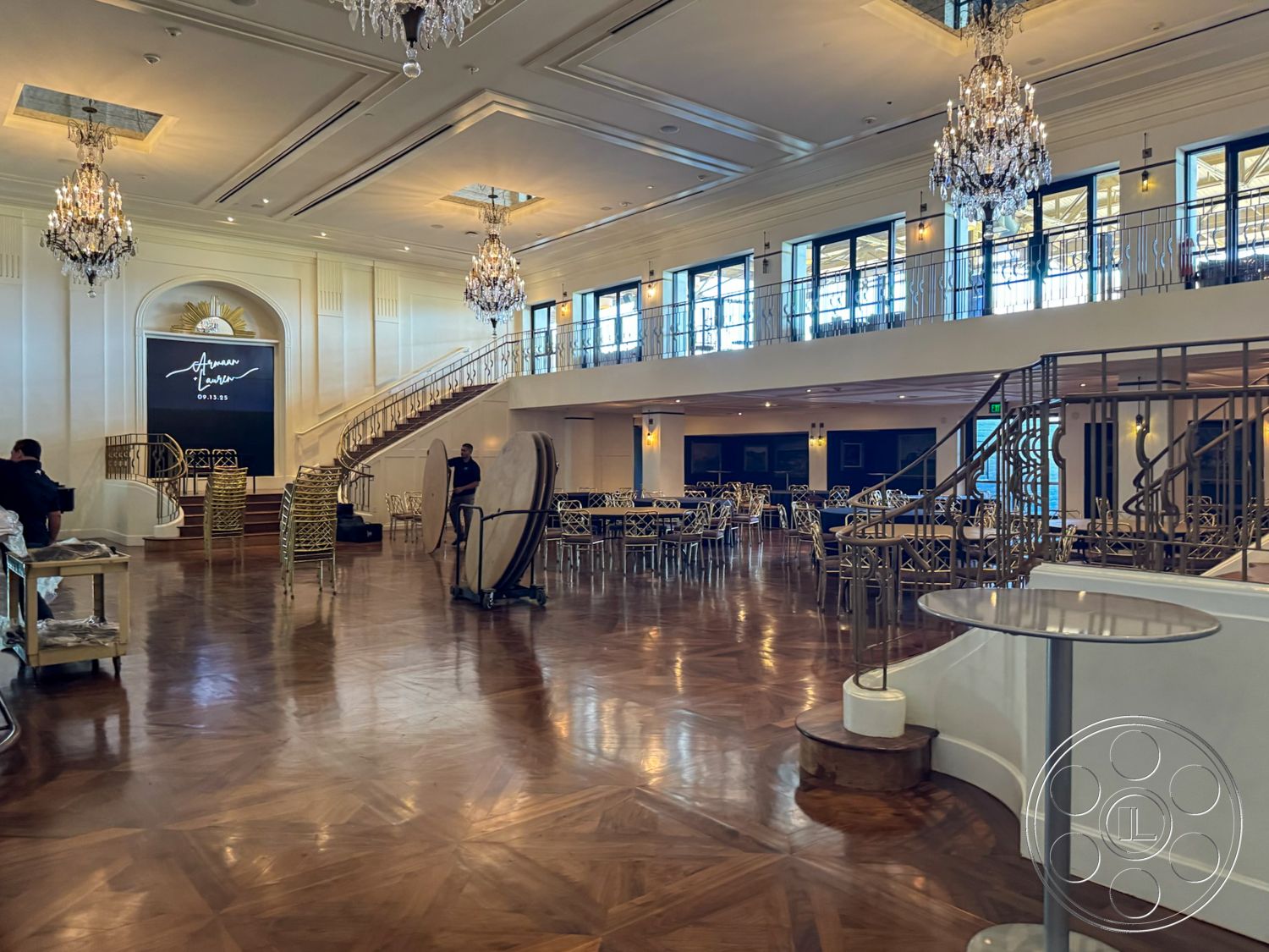 Arcadia Race Track - floor-to-ceiling windows, textured plaster walls, ambient recessed lighting, chandelier lighting fixtures, interior wooden parquet flooring, coffered high ceiling, curved staircase with decorative railing, white wainscoting details, built-in stage area, elegant event space, gold accents on furniture, modern art backdrop, open banquet area, stylish seating arrangements, classic ballroom atmosphere, luxurious finishing touches