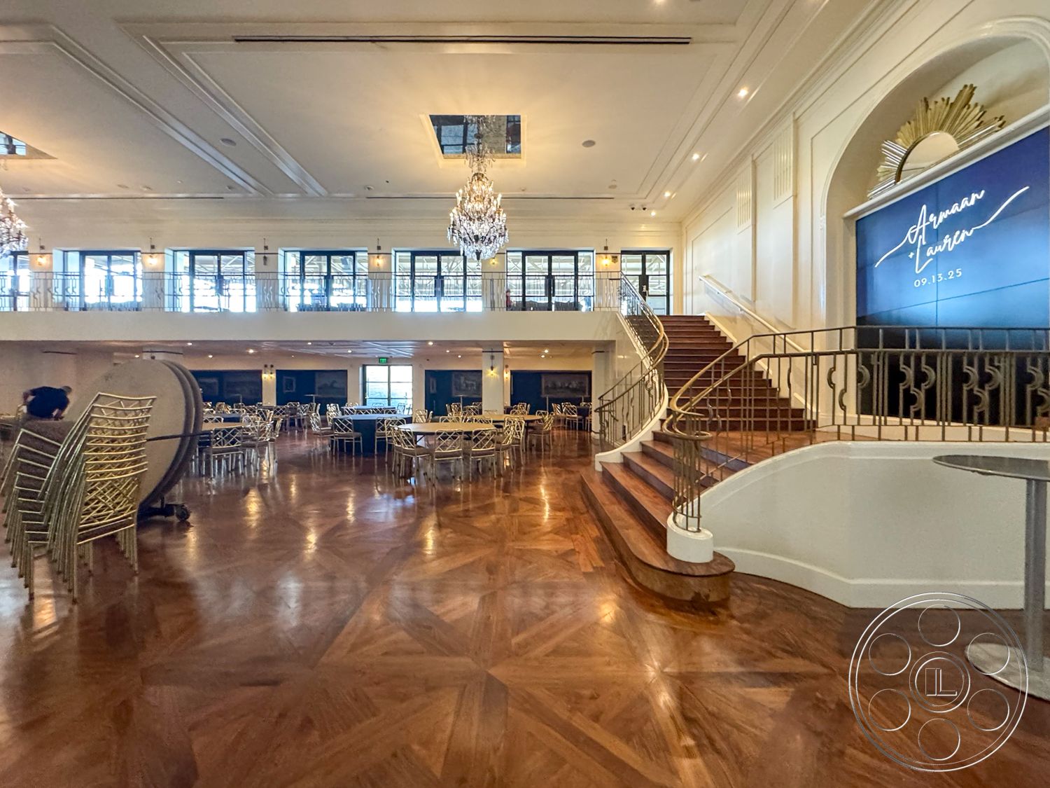 Arcadia Race Track - open space layout, large floor-to-ceiling windows, white plaster walls, decorative wall paneling, ornate ceiling moldings, natural light ambiance, herringbone hardwood flooring, curved wooden staircase, exterior landscaping view, sophisticated lighting design, chandelier lighting fixtures, metal railing with decorative details, event space interior, geometric patterned wall accents, parquet wood flooring design, modern event hall, luxury banquet area, elegant reception venue