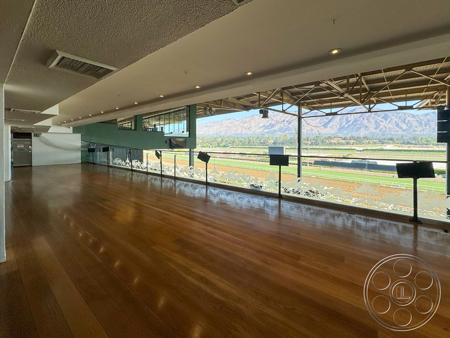 Arcadia Race Track - natural light interior, neutral painted walls interior, hardwood flooring interior, open floor plan interior, contemporary design interior, exposed metal support beams interior, glass railing with decorative elements interior, large panoramic windows interior, modern ceiling lighting fixtures interior, view of horse racing track exterior, mountain view exterior, spacious gathering area interior, urban architecture exterior, athletic facility interior, functional space for events interior