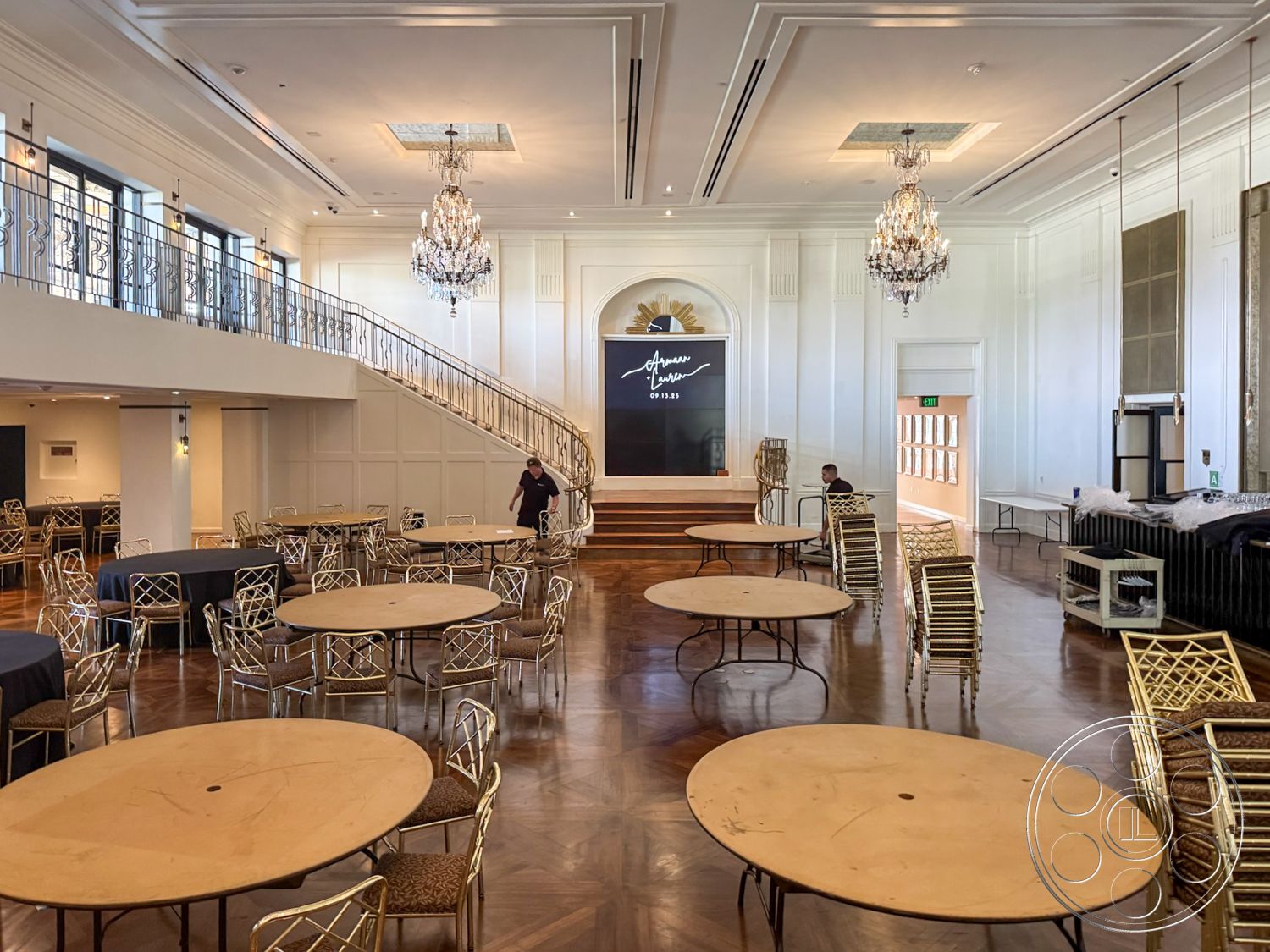 Arcadia Race Track - interior space, reception area, accessible entrance, crown molding details, polished hardwood flooring, natural light-filled room, round wooden dining tables, dark wood paneling accents, exposed wooden beams in ceiling, chandelier lighting fixtures, geometric patterned wood inlays, curved staircase with wrought iron railings, white wainscoting panel walls, golden lattice-back chairs, stage area with black backdrop, large windows with decorative grills, open event space, multi-functional gathering place, elegant banquet hall, sophisticated décor