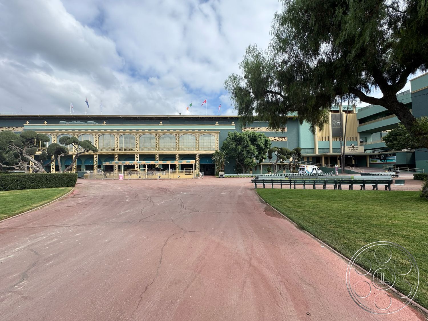 Arcadia Race Track - exterior, brick facade, paved walkway, outdoor seating areas, modern architectural style, asphalt driveway, ornamental trees, open entryway, glass storefront windows, landscaped lawn area, metal decorative railings, green-colored exterior walls, circular planter beds, equine sculpture feature, flagged entrances