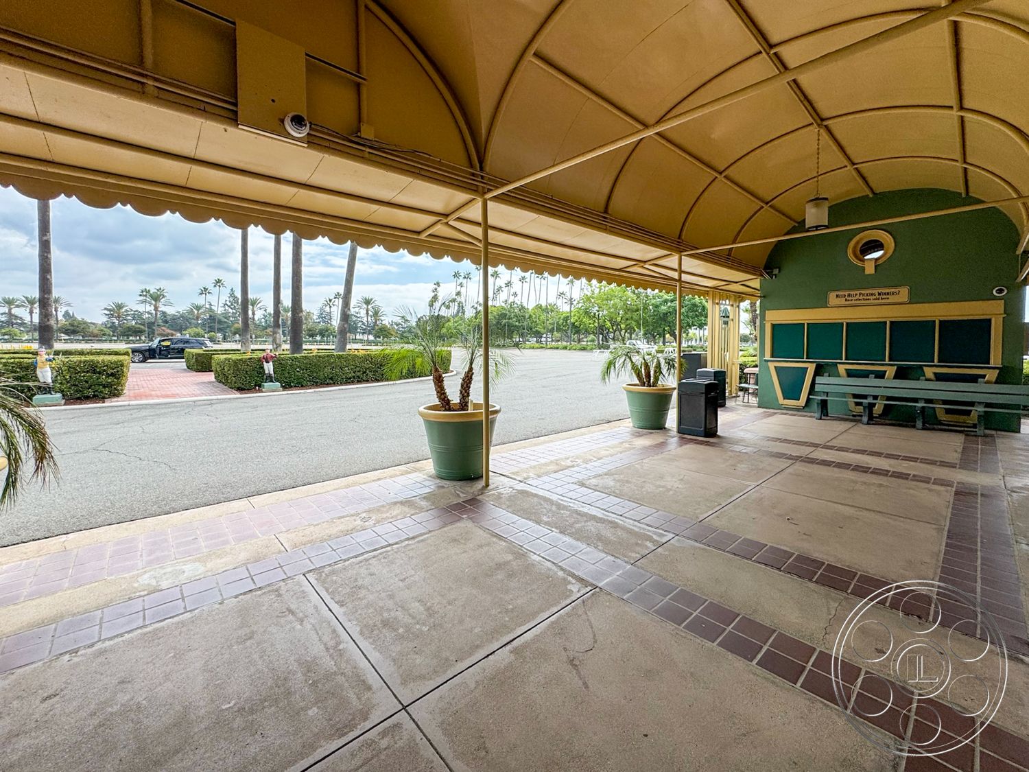 Arcadia Race Track - surrounding greenery, paved walkway, park-like setting, poolside view, palm tree landscaping, exterior patio flooring, modern outdoor design, concrete patio tiles, public gathering space, colored concrete walkways, arched canopy roof, green feature wall, urban outdoor seating area, planted flower pot decor, tile decorative border, open-air market space, commercial outdoor area, city parking lot view, covered waiting area, decorative trash receptacles