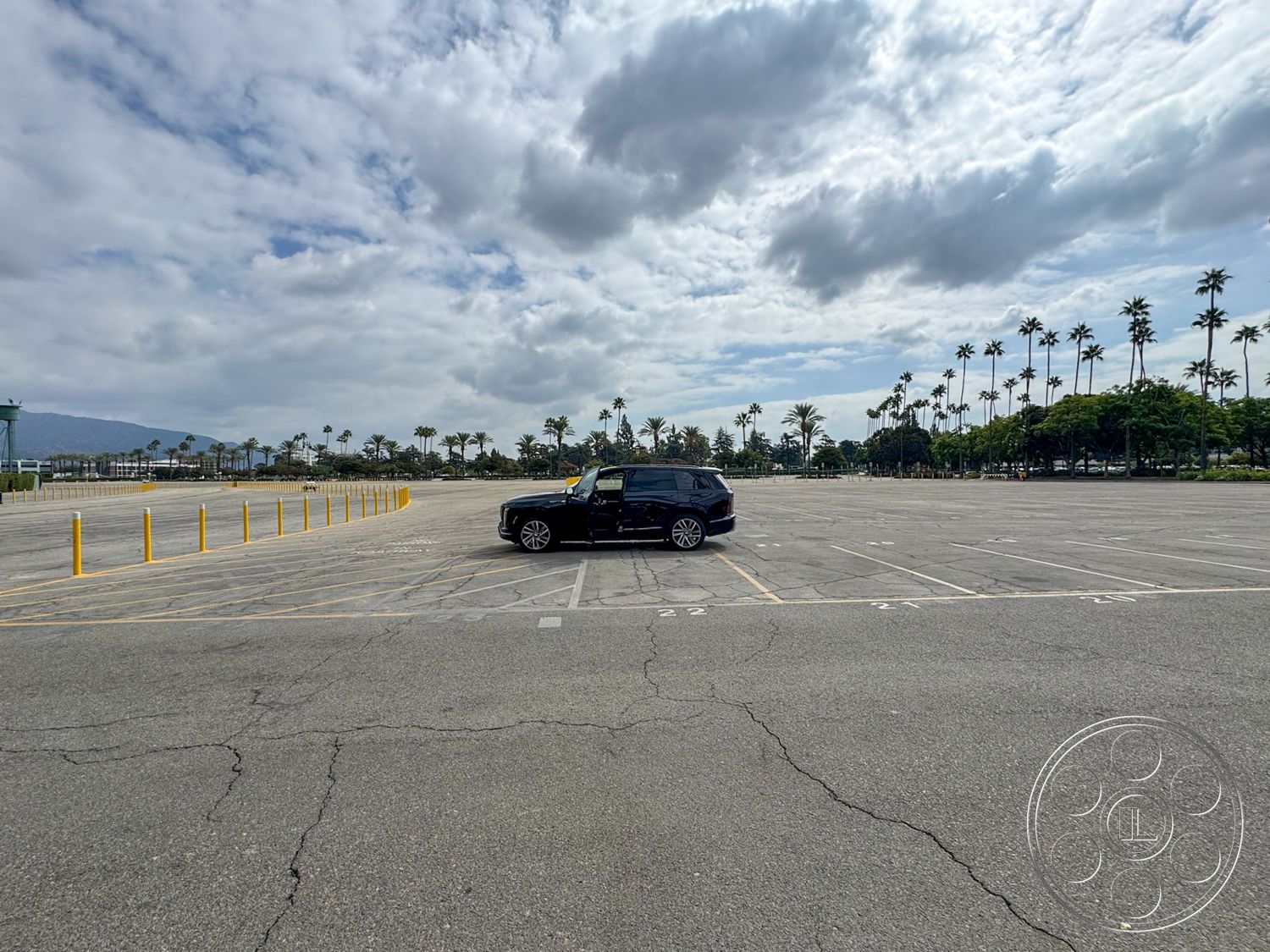 Arcadia Race Track - surrounding greenery, urban setting, outdoor area, city skyline view, paved surface, commercial area, vehicular access, asphalt parking lot, access road, empty parking spaces, palm tree landscaping, cloudy sky backdrop, yellow raised bollards, open space environment, concrete curb