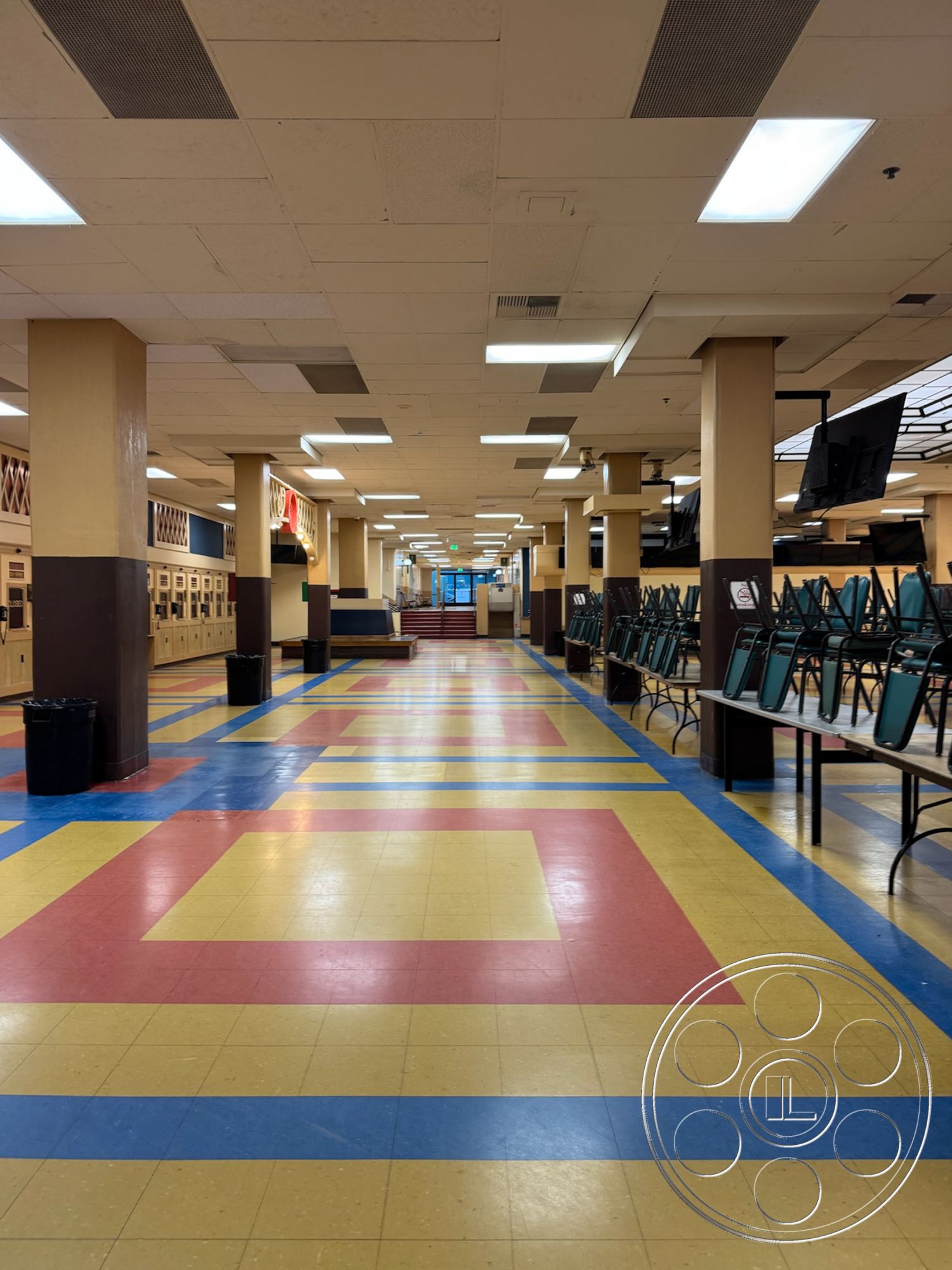 Arcadia Race Track - exposed ceiling panels, interior corridor, fluorescent ceiling lights, modern classroom design, yellow vinyl floor tiles, tile flooring with geometric patterns, red and blue accent tiles, wooden lockers, open seating area