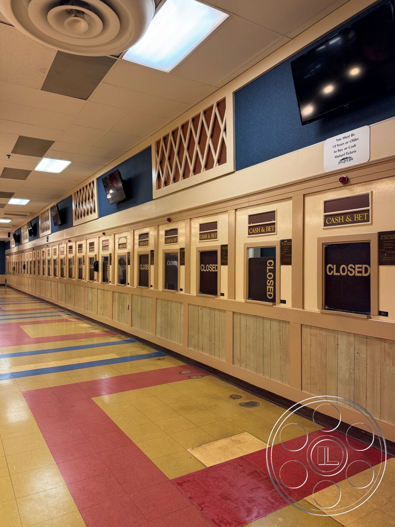 Arcadia Race Track - waiting area, commercial interior, recessed lighting fixtures, wood paneling wall treatment, linoleum tile flooring, interior betting counter area, multicolored floor tiles, blue acoustic ceiling tiles, decorative wood lattice accents, flat panel television screens, closed betting windows, cashier's station, gambling facility design, rectangular counters, public venue ambience