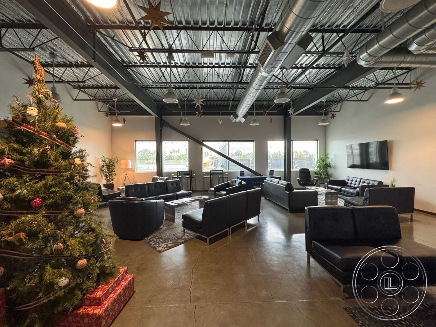 HW Hangar - decorative area rug, interior space, modern coffee table, floor-to-ceiling windows, exposed ductwork, black leather sofas, contemporary lounge area, open-concept living area, neutral wall paint, glass wall partition, large windows with city view, industrial-style ceiling, decorative holiday decor, concrete polished floors, artificial Christmas tree, minimalist light fixtures, steel awning over windows, uplighting accents, contemporary desk chairs, rustic wooden side table