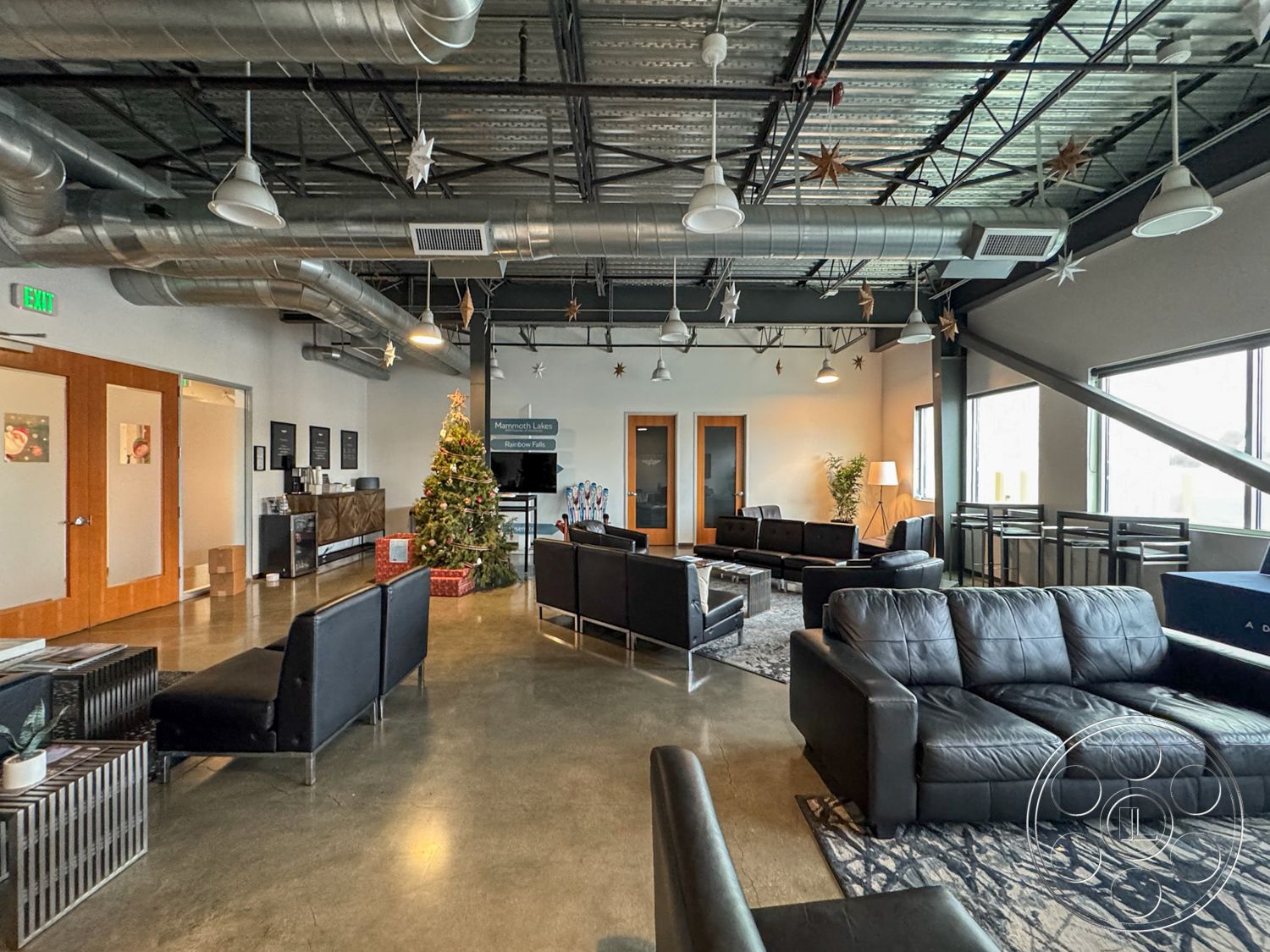 HW Hangar - textured area rug, polished concrete flooring, open concept layout, floor-to-ceiling windows, industrial design elements, decorative Christmas tree, metal light fixtures, glass wall partitions, black leather sofas, interior lounge area, modern lounge seating, exposed ductwork ceiling, urban office setting, steel structural beams, contemporary coffee tables, wooden door accents
